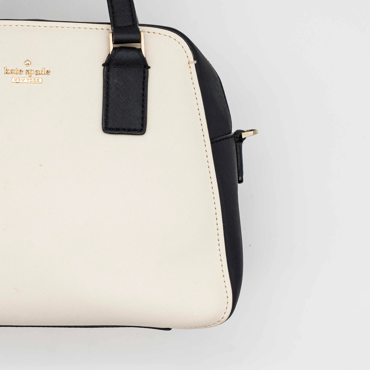 Kate Spade Cameron Street Little Babe satchel in black and white leather with gold hardware, shown with dual handles against a minimal background.