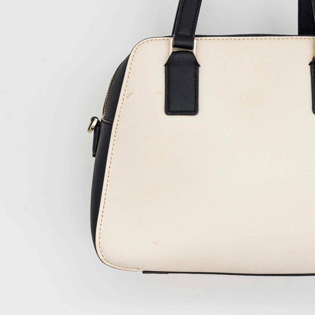 Kate Spade Cameron Street Little Babe satchel in black and white leather with gold hardware, shown with dual handles against a minimal background.