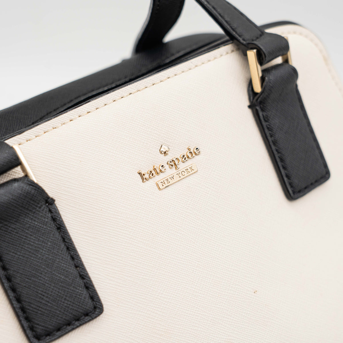 Kate Spade Cameron Street Little Babe satchel in black and white leather with gold hardware, shown with dual handles against a minimal background.