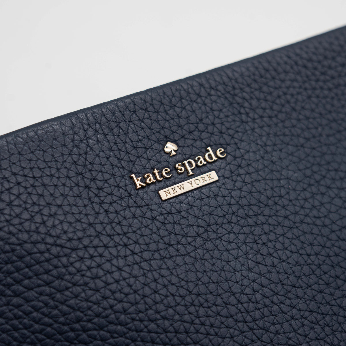 Kate Spade navy blue crossbody bag in pebbled leather, shown with adjustable strap and gold-tone accents.