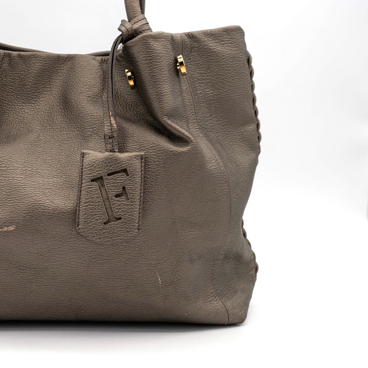 Furla taupe leather shoulder bag with gold hardware and braided detailing, photographed against a white background.