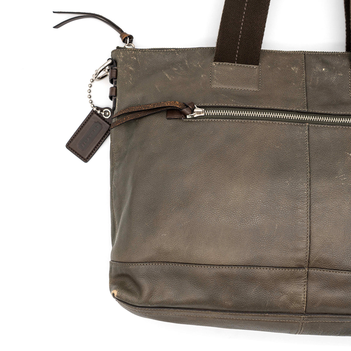 Coach brown leather tote bag with double handles and front zip pocket, shown on a white background.