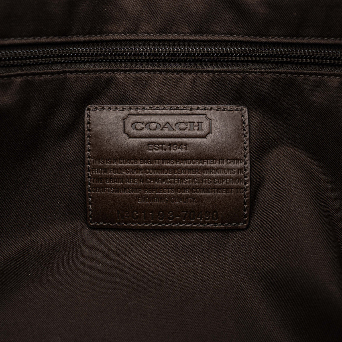 Coach brown leather tote bag with double handles and front zip pocket, shown on a white background.