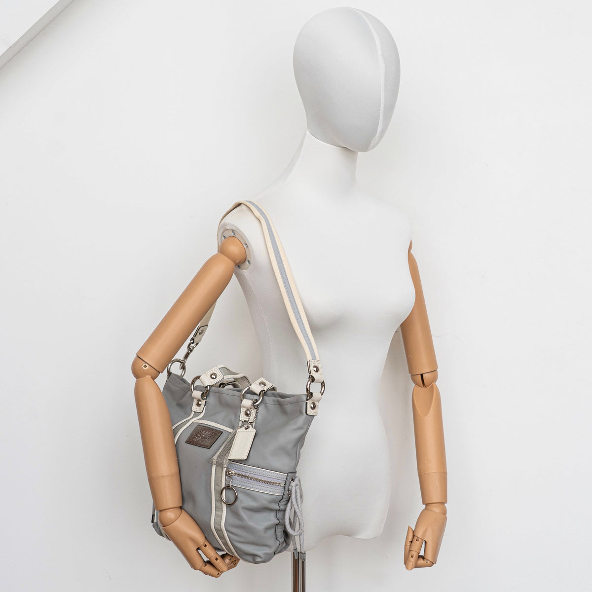 Coach Poppy Spotlight grey shoulder bag with double top handles, white trim, and detachable webbing strap, displayed on a white background.
