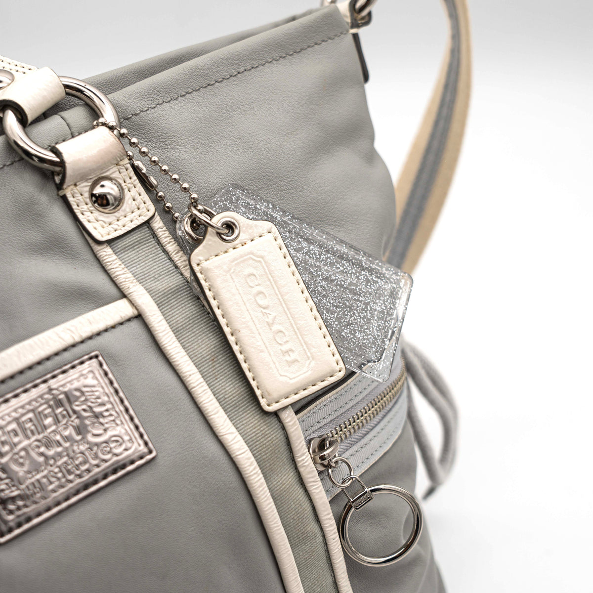 Coach Poppy Spotlight grey shoulder bag with double top handles, white trim, and detachable webbing strap, displayed on a white background.