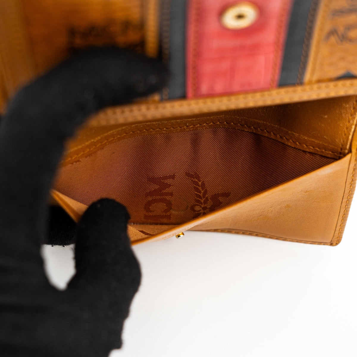 Front view of the MCM Cognac Visetos Monogram Stripe Trifold Wallet in brown with red and black accents and gold logo plaque.
