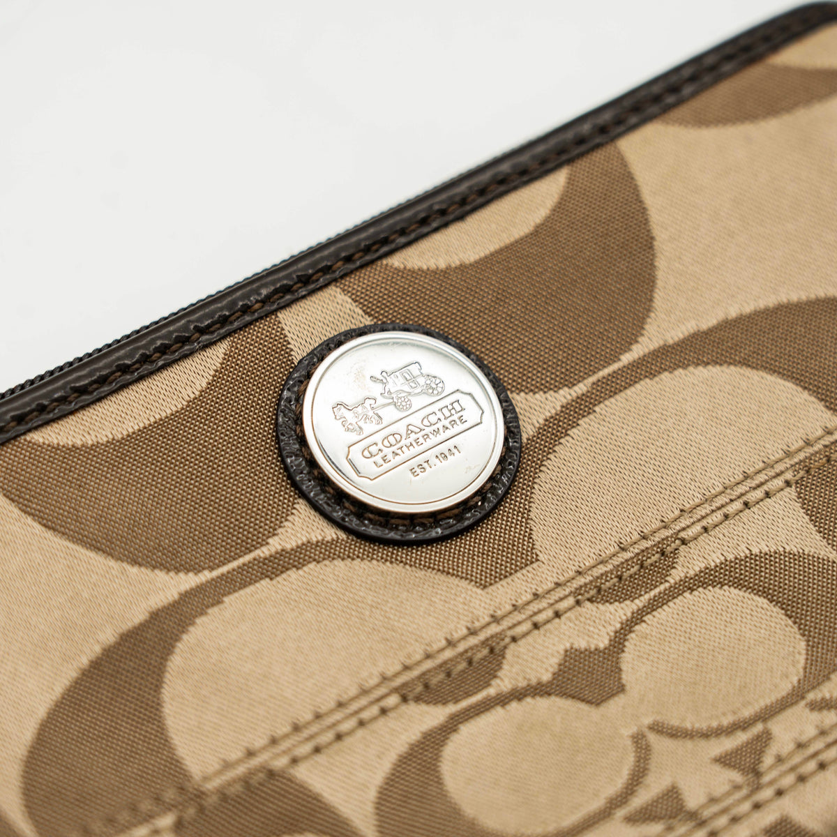 Coach brown monogram wristlet with silver badge and detachable leather strap, photographed on a white background.