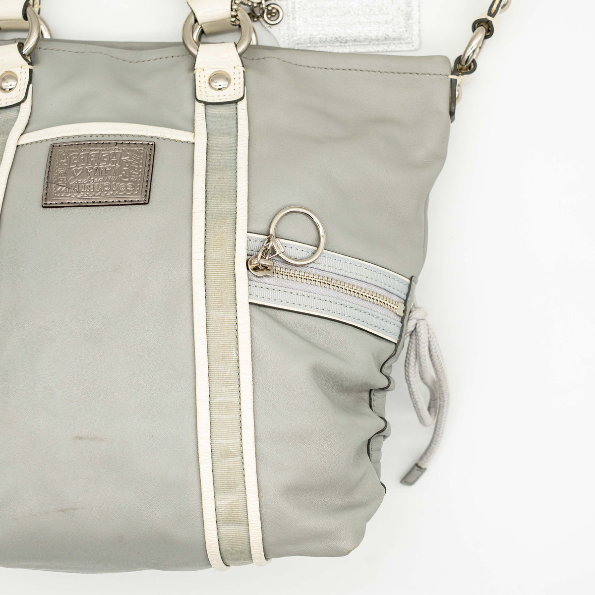 Coach Poppy Spotlight grey shoulder bag with double top handles, white trim, and detachable webbing strap, displayed on a white background.