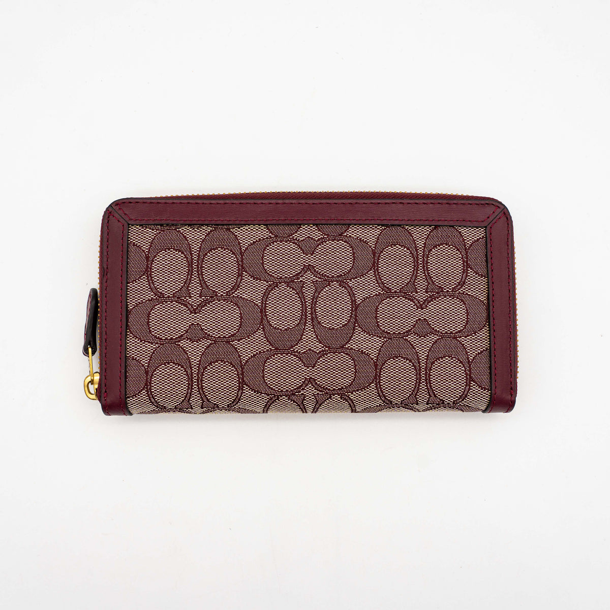 Coach Signature Accordion Zip Wallet in burgundy monogram canvas with leather trim and gold zip, photographed against a clean white background.