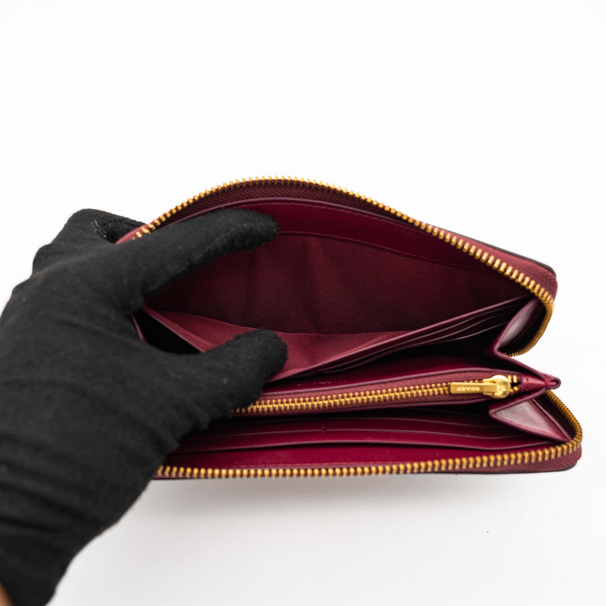 Coach Signature Accordion Zip Wallet in burgundy monogram canvas with leather trim and gold zip, photographed against a clean white background.