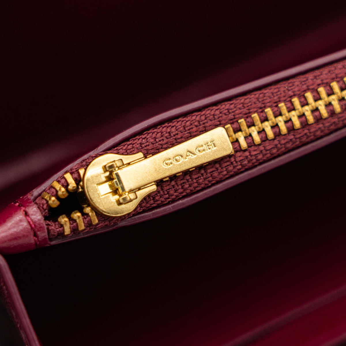 Coach Signature Accordion Zip Wallet in burgundy monogram canvas with leather trim and gold zip, photographed against a clean white background.