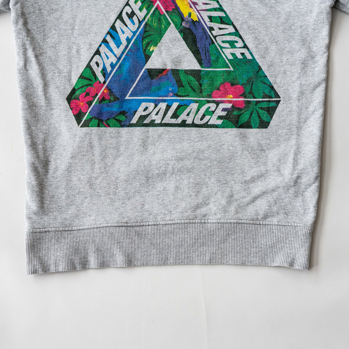Palace grey pullover hoodie with tropical Tri-Ferg back graphic and white chest logo, laid flat on a neutral background.