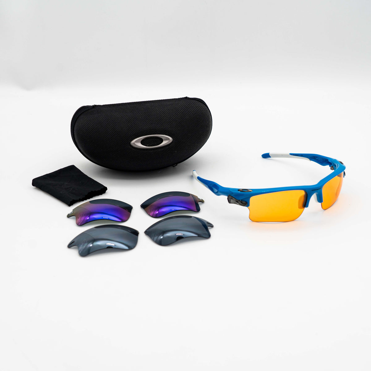 Oakley Fast Jacket OO9156-04 sunglasses in blue with orange lenses, displayed with two extra pairs of lenses, cleaning cloth and a black Oakley hard case.