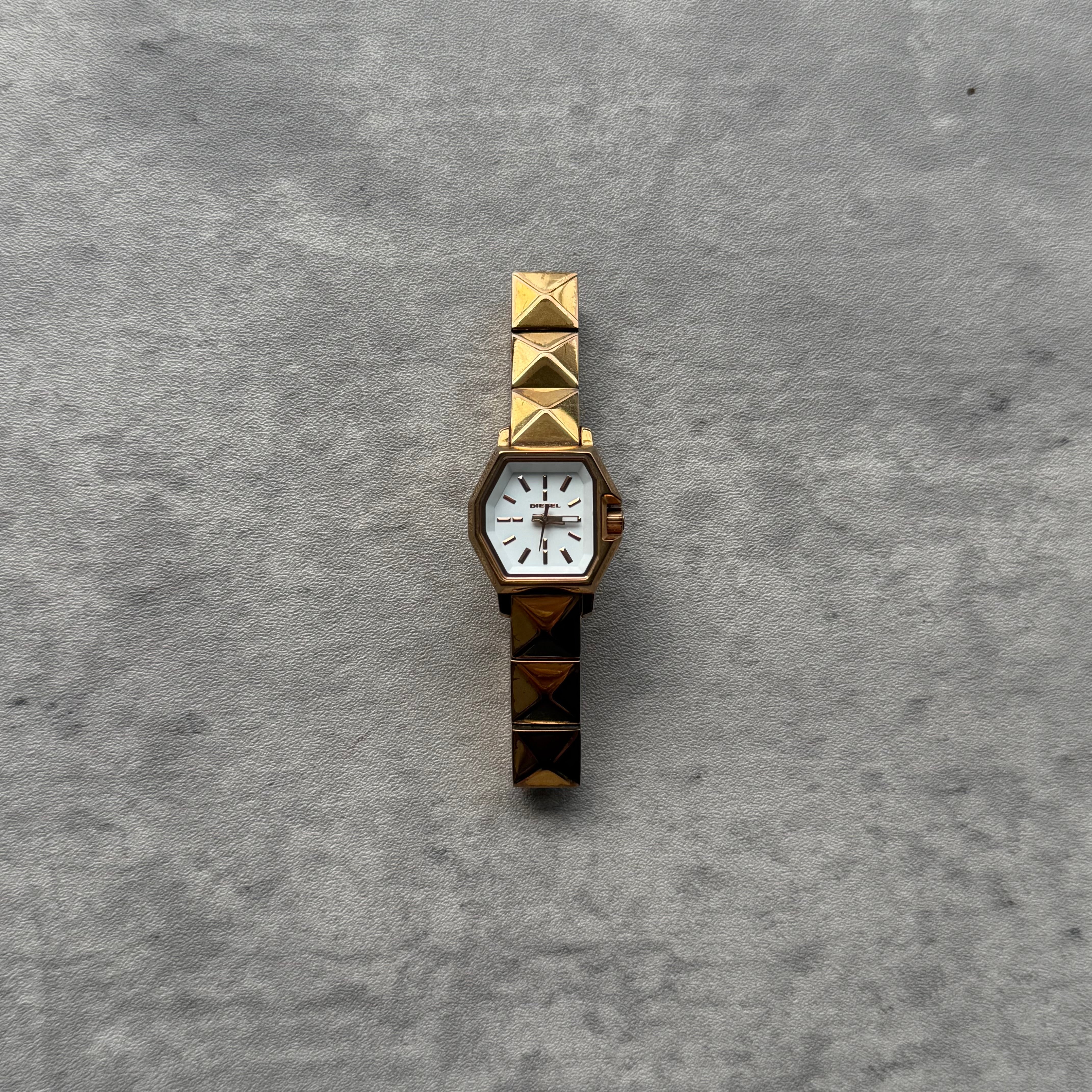 Diesel DZ-5299 Vintage Gold Watch with hexagonal white dial, gold-tone hands, and pyramid-studded bracelet.
