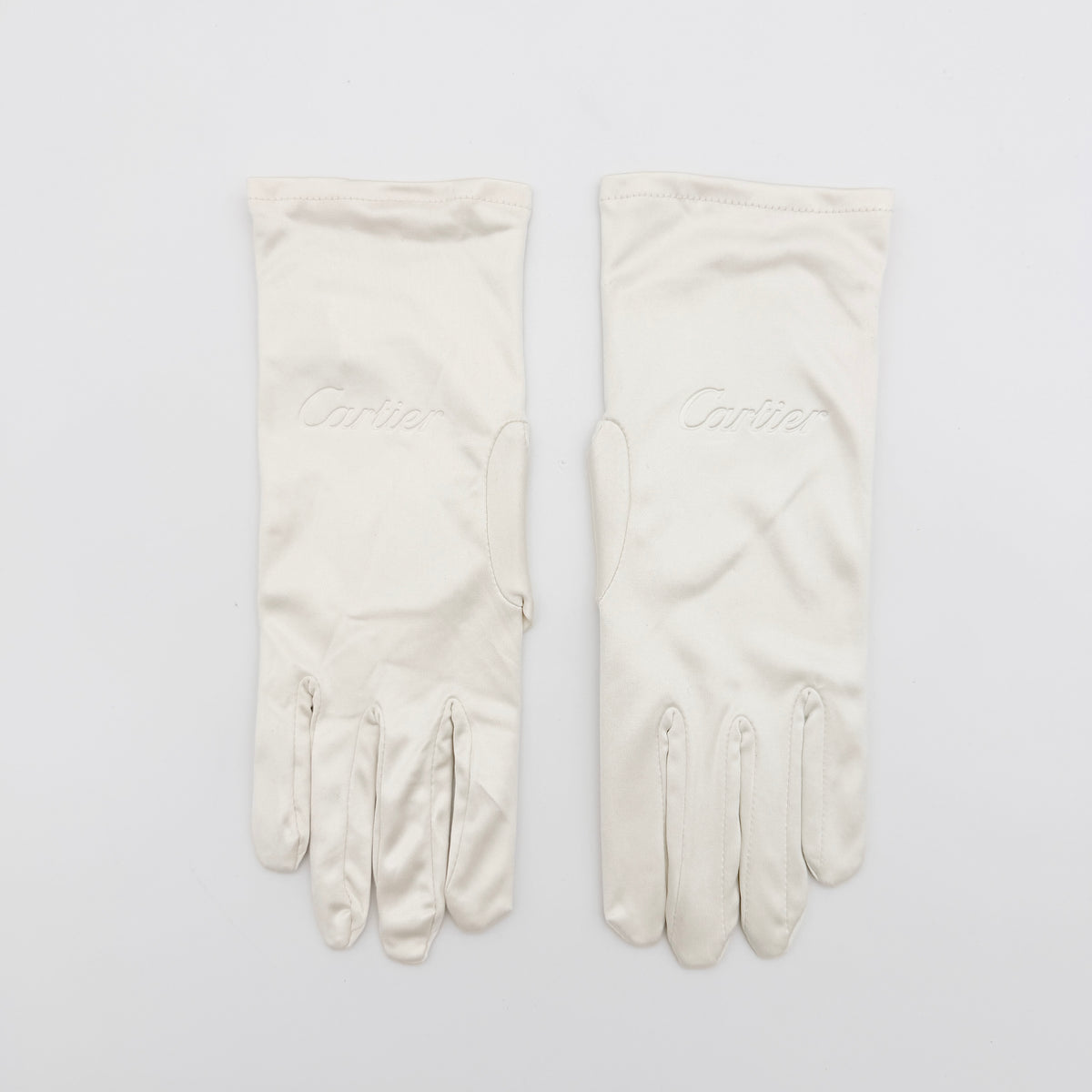 Pair of Cartier ivory gloves with signature script logo embroidery displayed on a flat white background.