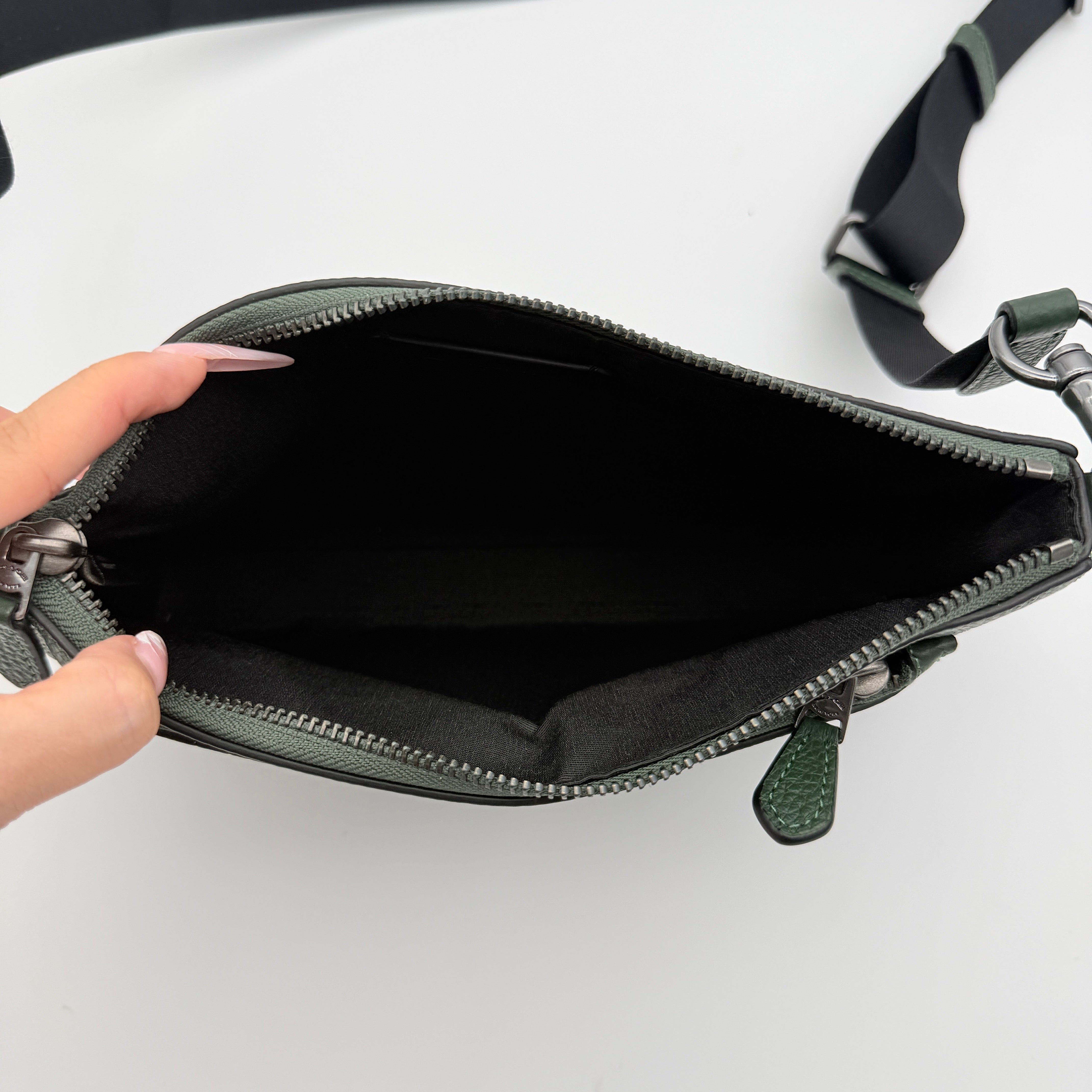 Coach Holden Crossbody bag in dark green pebbled leather with adjustable black webbing strap, displayed against a white background.