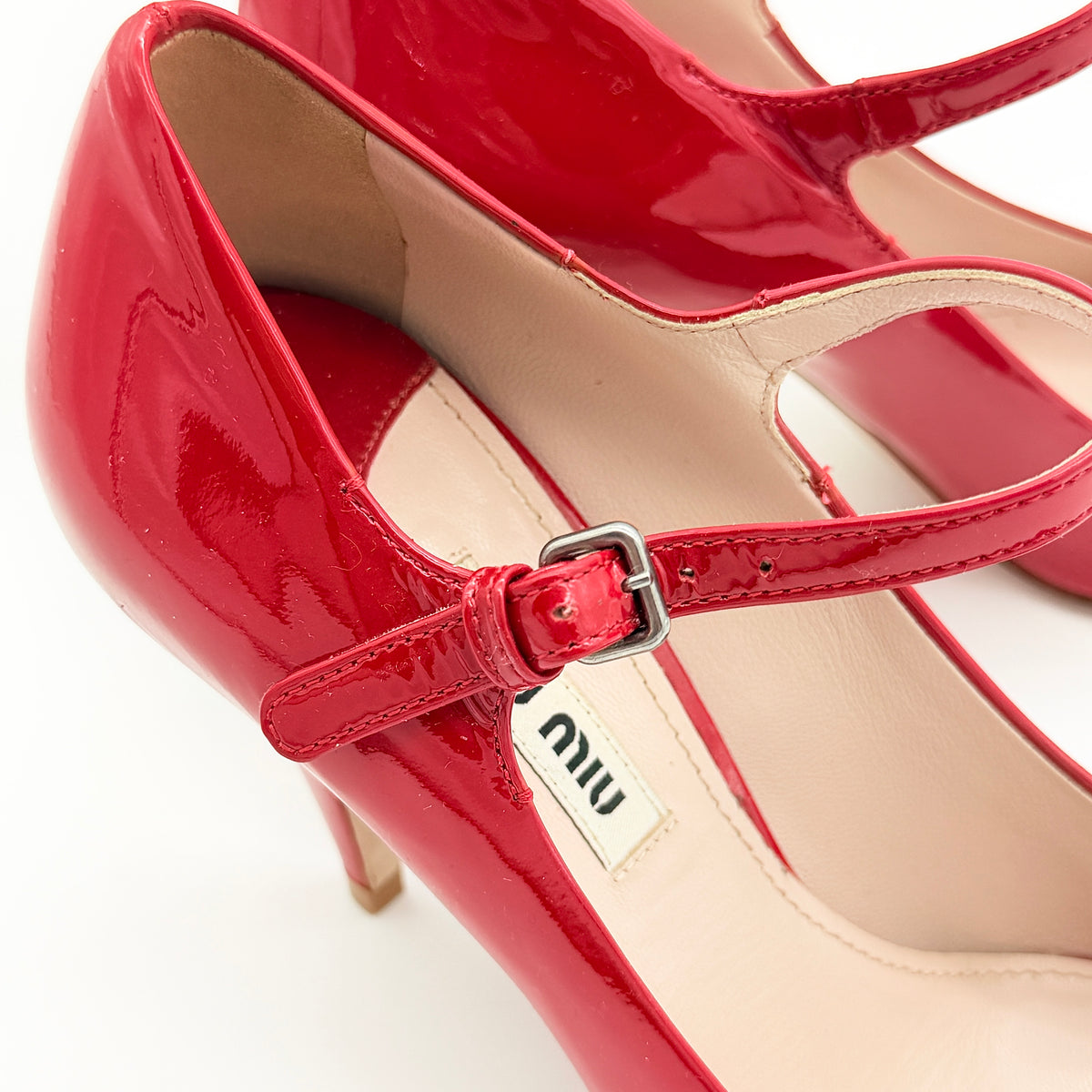 A pair of red patent leather Miu Miu Mary Jane heels with adjustable buckle straps and high heels, displayed against a white background.