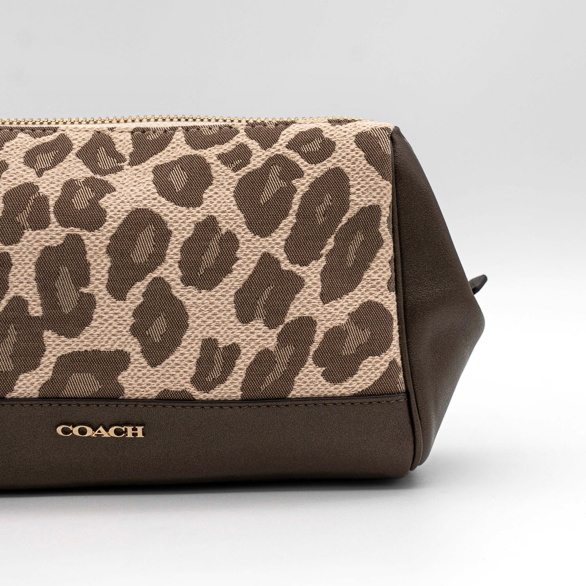 Coach cosmetic pouch in brown and beige leopard print canvas with chocolate leather trim and gold hardware, shown with wrist strap.