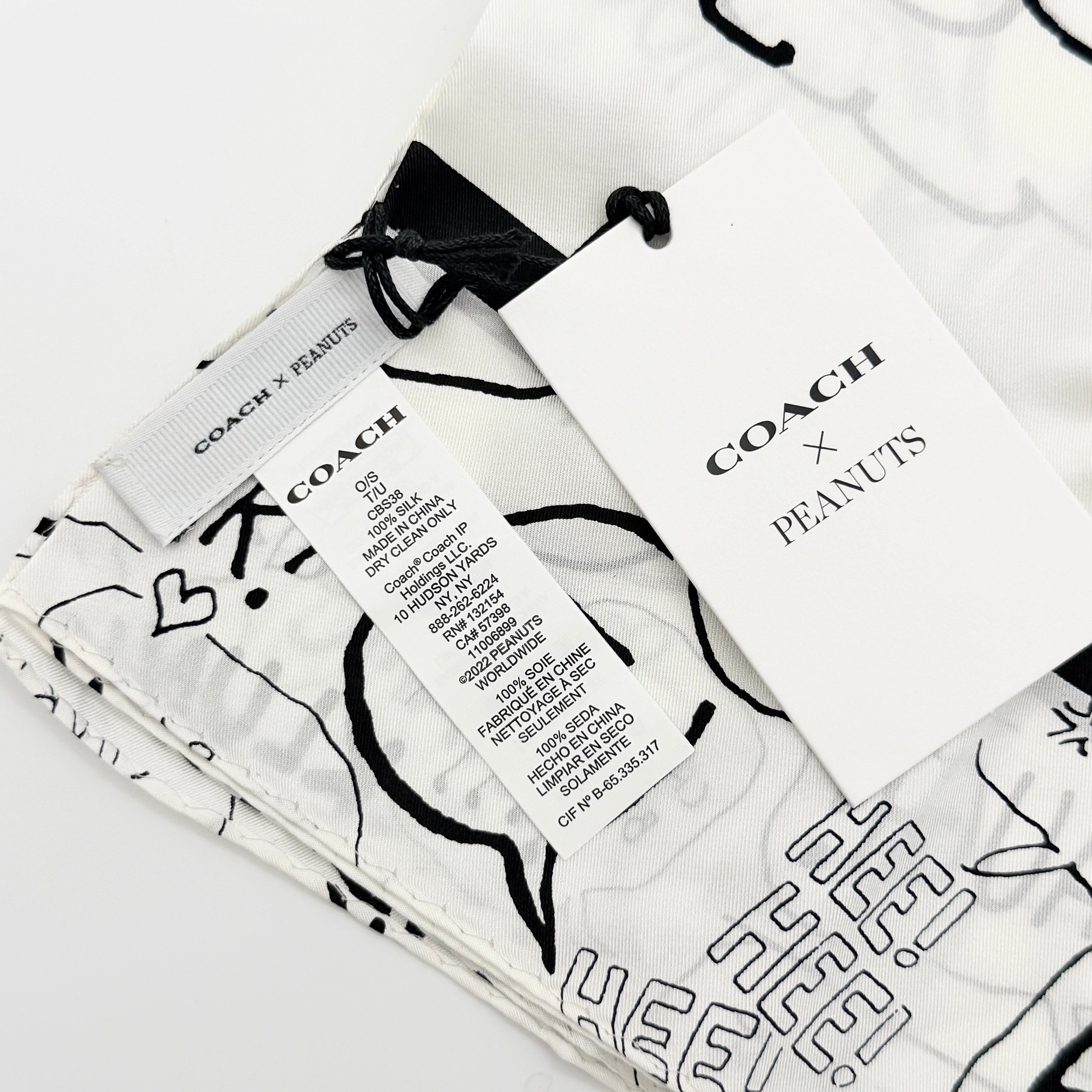 Coach x Peanuts black and white silk scarf featuring a Snoopy surfing comic print, shown with Coach packaging and tags.
