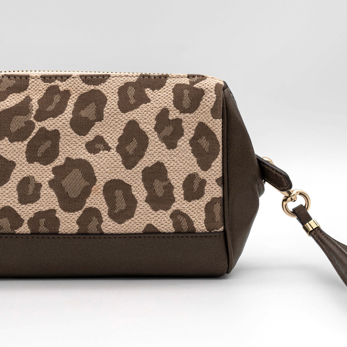 Coach cosmetic pouch in brown and beige leopard print canvas with chocolate leather trim and gold hardware, shown with wrist strap.