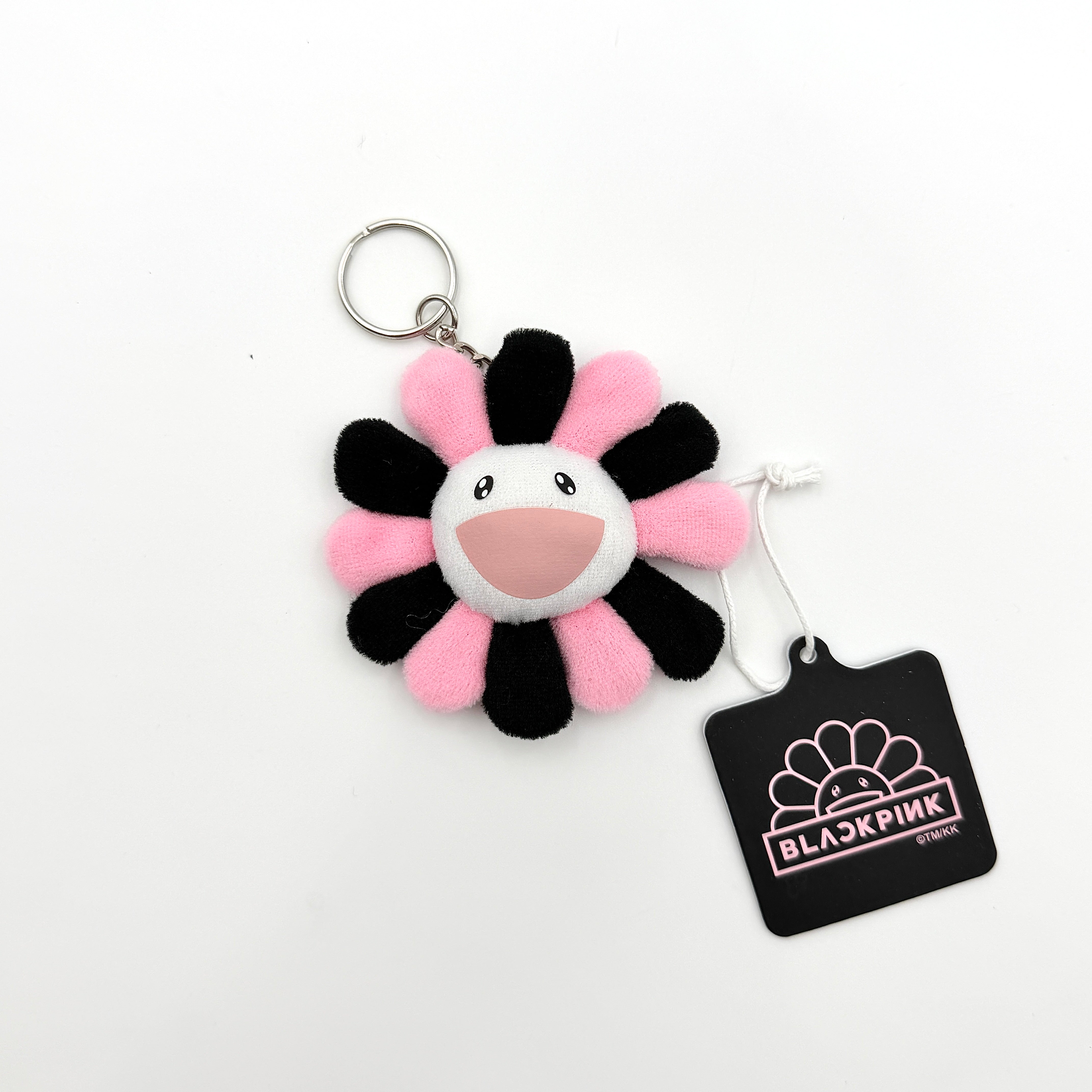 Takashi Murakami x BLACKPINK plush flower keychain in black and pink with smiling face and branded tag.
