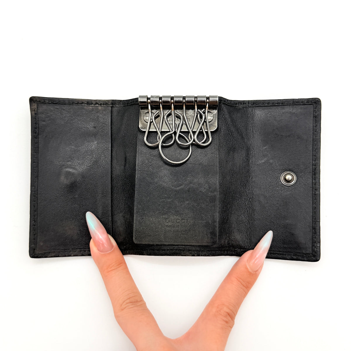 Gucci Guccissima GG Monogram black leather key case with silver-tone hardware, shown closed against a white background.