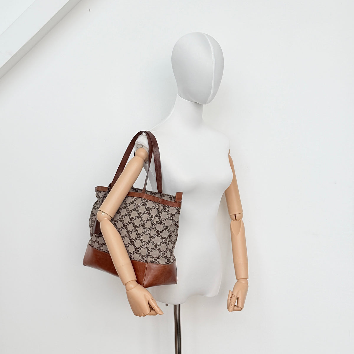 Celine Triomphe Macadam Canvas Tote Bag in beige and brown with leather trim and top handles, styled against a white background.