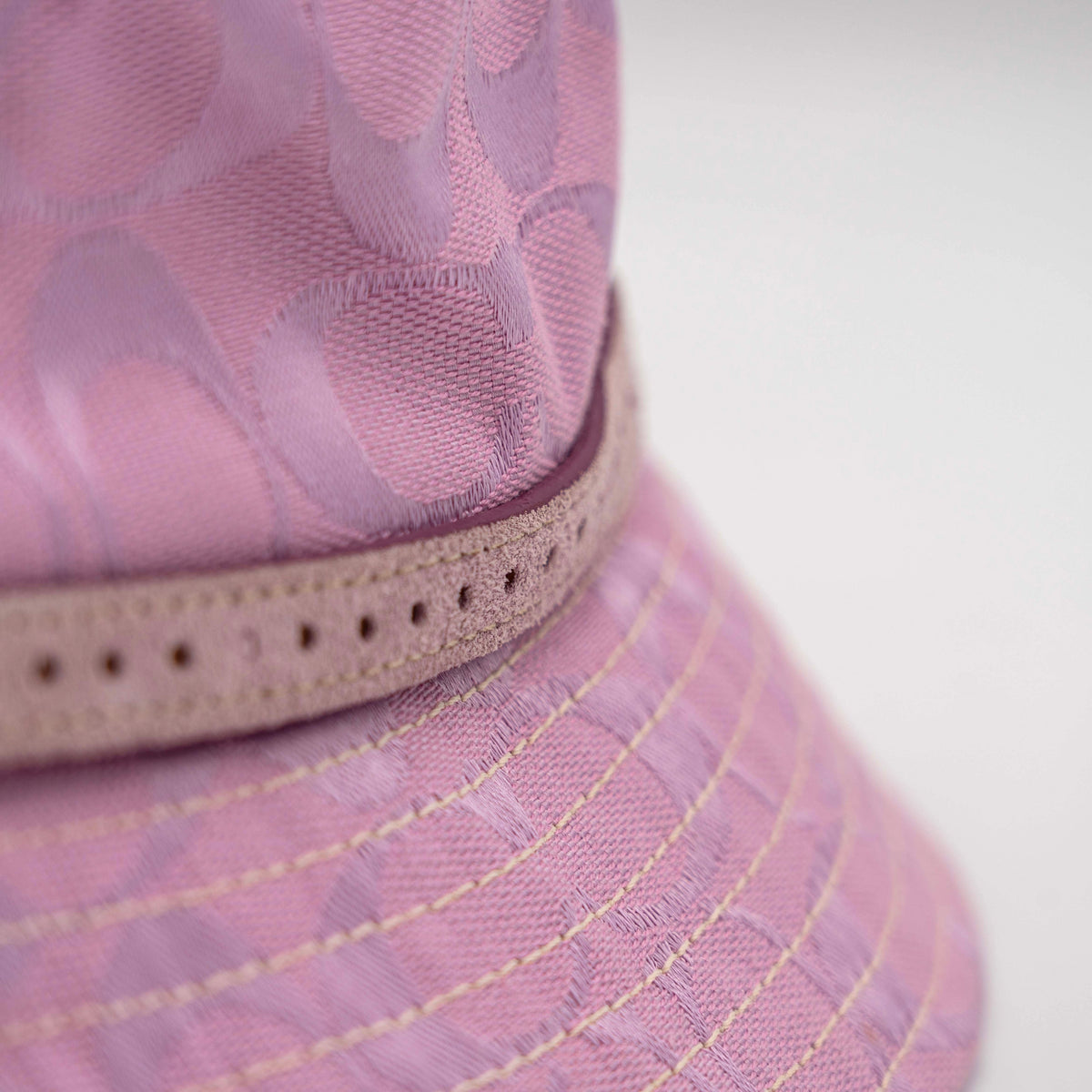 Coach pink jacquard bucket hat with taupe suede-effect band, shown against a neutral background.