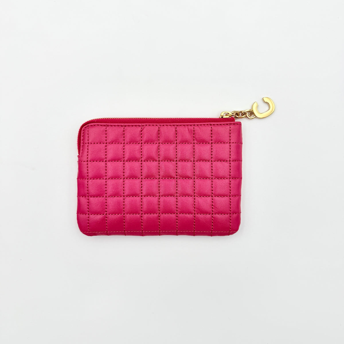 Celine quilted pink coin and card wallet with gold C charm, displayed on a black Celine dust bag.
