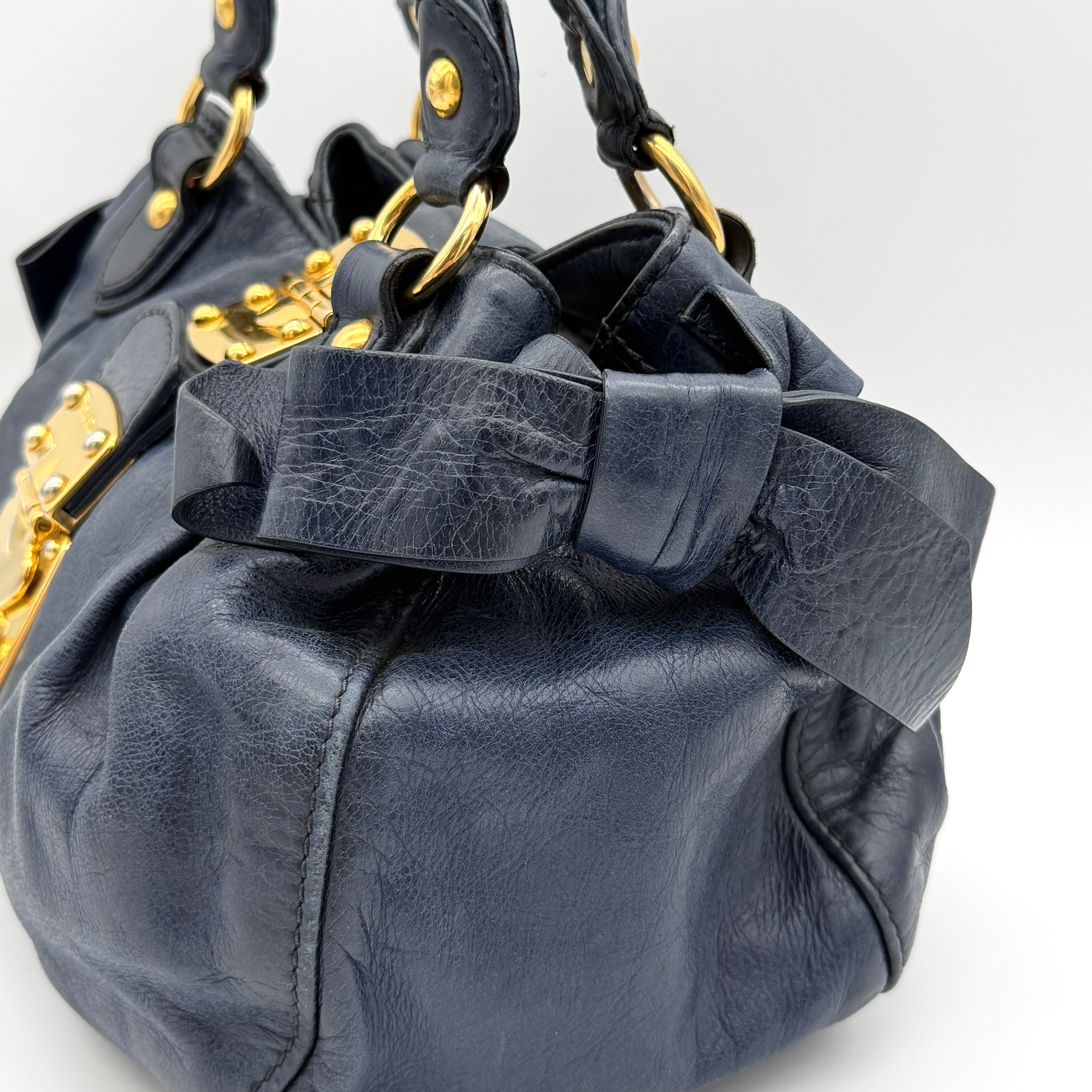 Miu Miu navy blue Vitello Lux Bow Satchel with gold-tone hardware, detachable strap, and dust bag.
