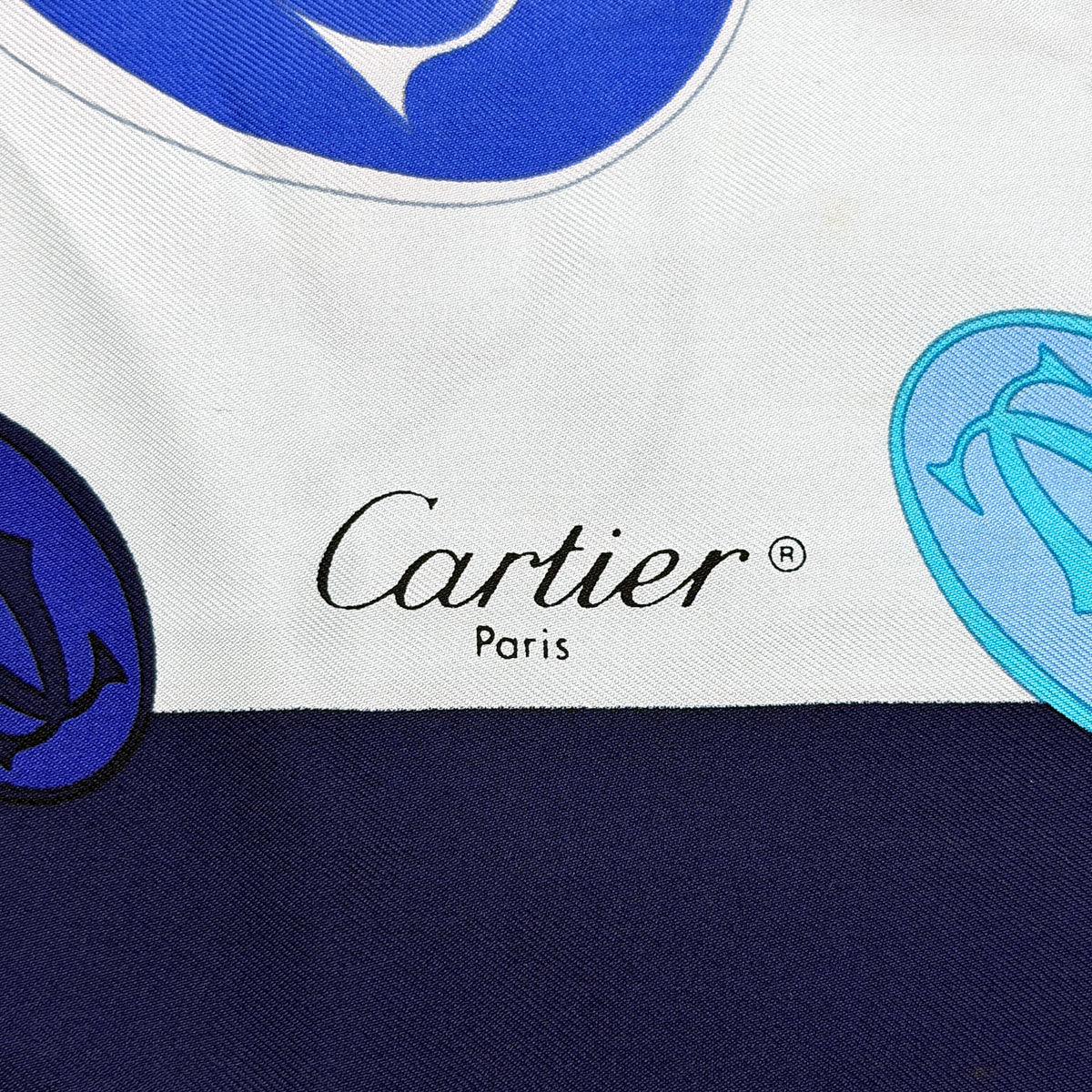 Cartier silk scarf in blue and white with graphic monogram logo print and navy border, elegantly arranged.