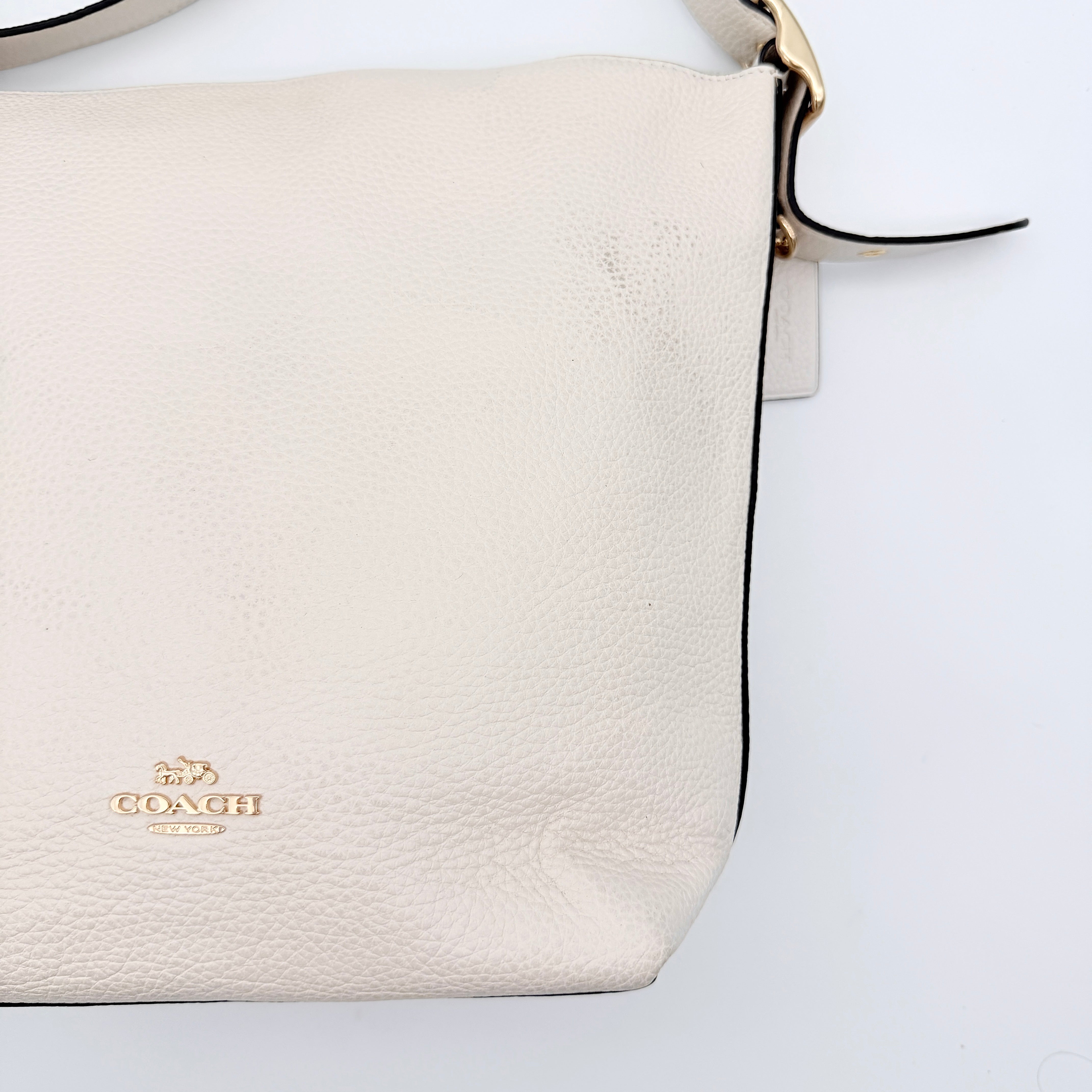 Coach Ellie File Crossbody Bag in ivory pebbled leather with gold hardware and adjustable strap, displayed on a white background.