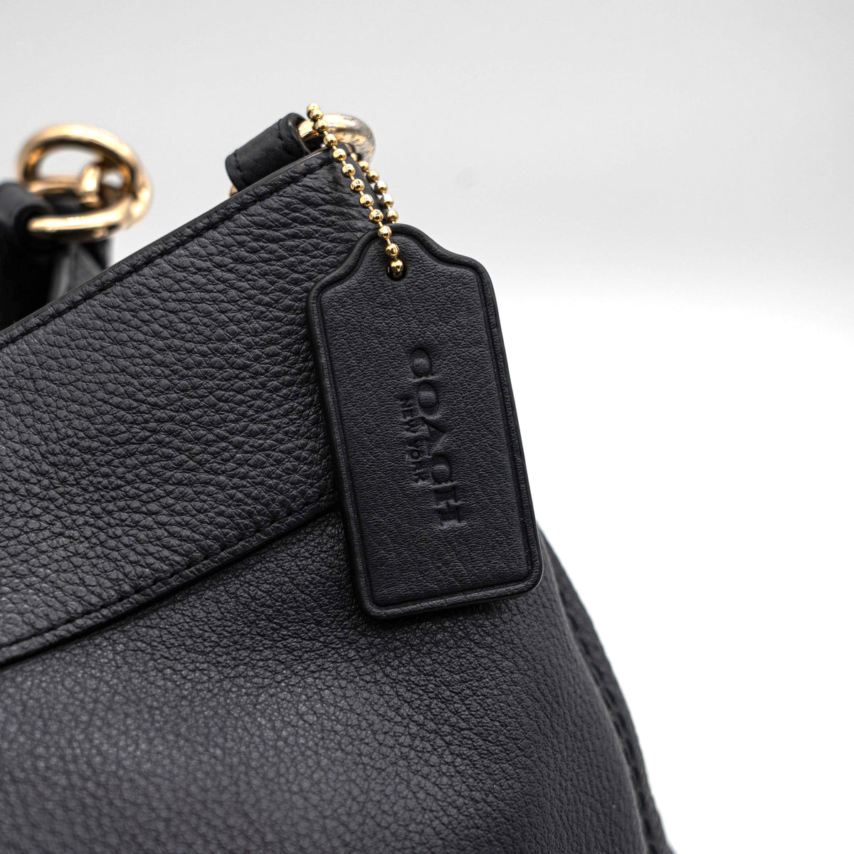 Coach Lexy Shoulder Bag in black pebbled leather with gold-tone hardware and double handles, styled against a white background.