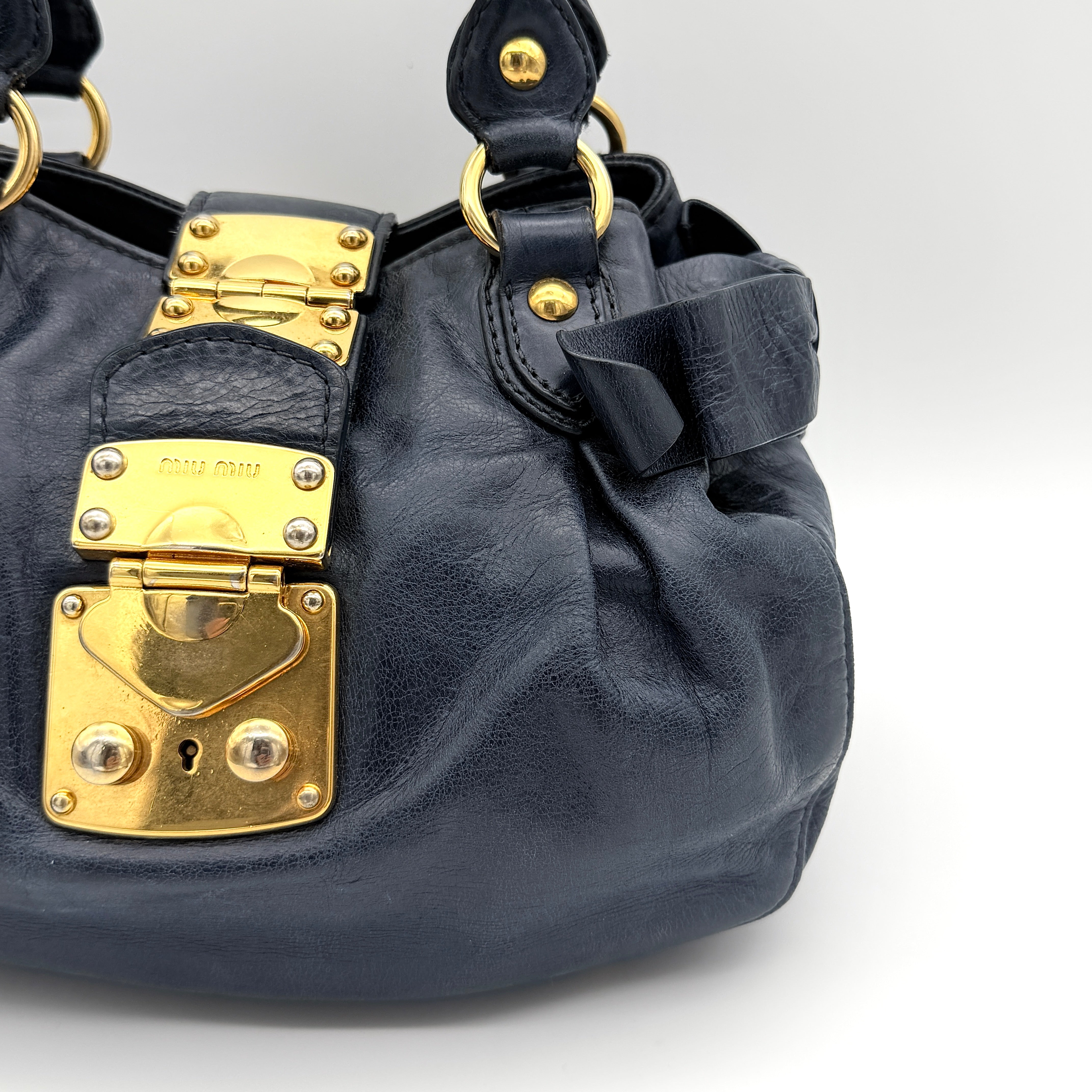 Miu Miu navy blue Vitello Lux Bow Satchel with gold-tone hardware, detachable strap, and dust bag.