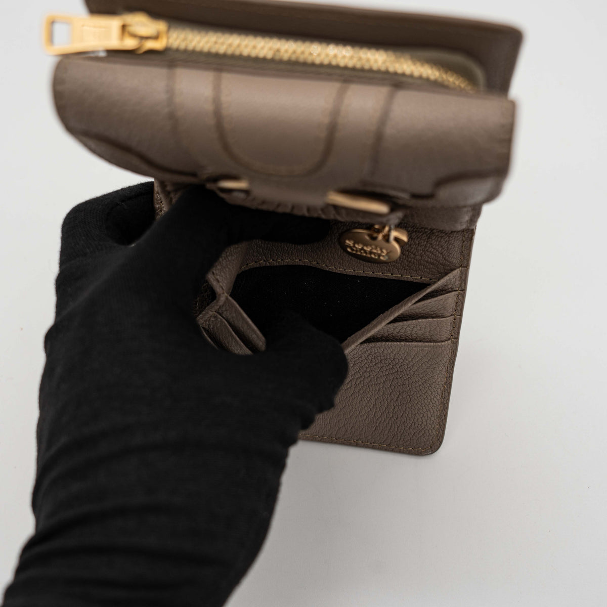 See by Chloe Hana tri-fold wallet in grey grained leather with gold-tone ring and charms, photographed closed on a white background.