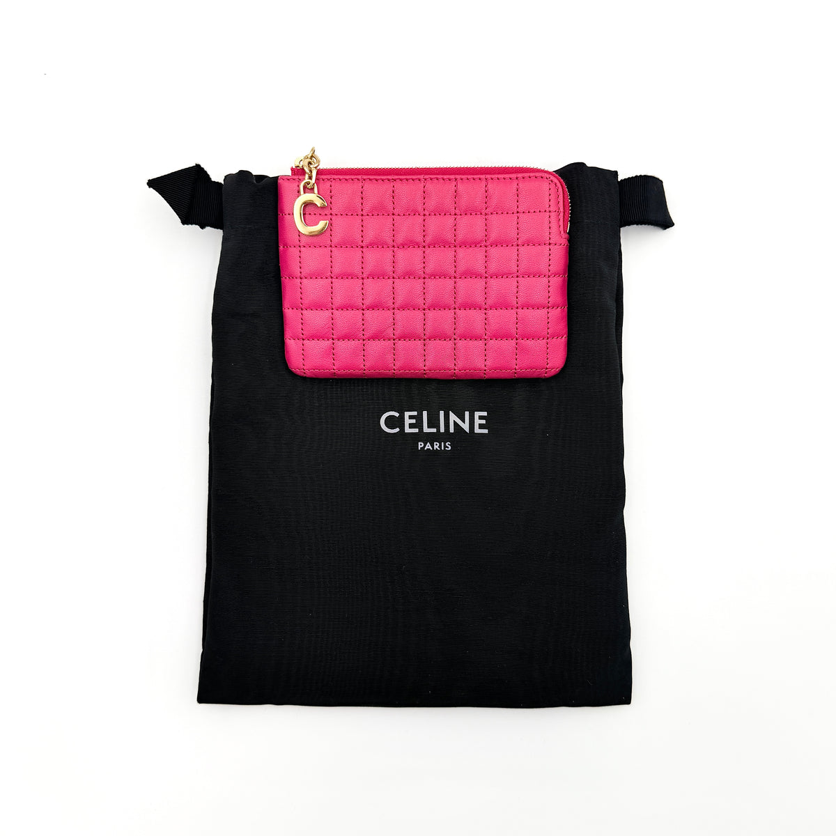 Celine quilted pink coin and card wallet with gold C charm, displayed on a black Celine dust bag.