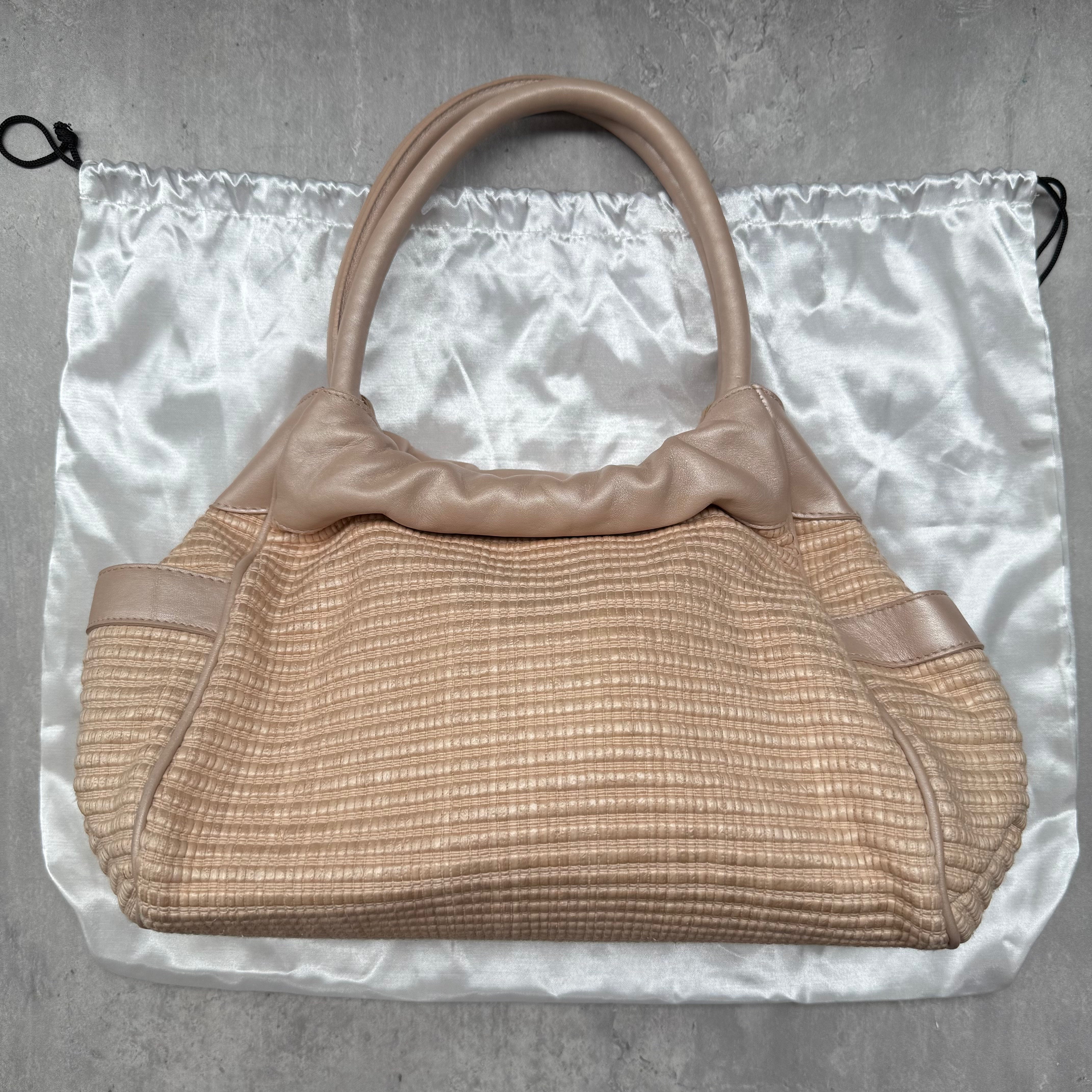 Furla Straw Tote Bag in woven straw with metallic rose gold leather trim and dual handles.