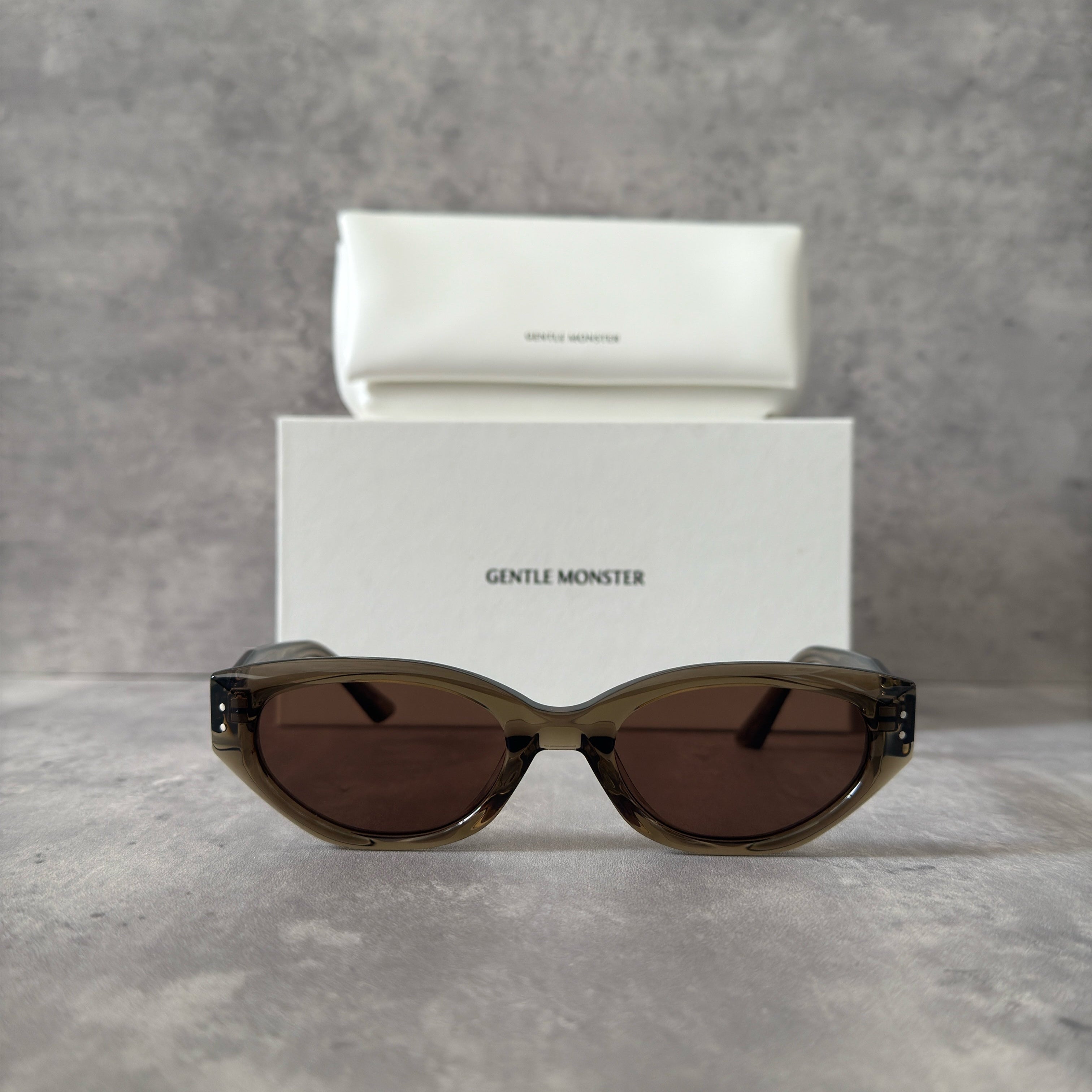 Gentle Monster ROCOCO KC6 sunglasses in translucent smoky brown acetate, featuring a bold sculpted design, tinted brown lenses, and signature metal temple detailing.