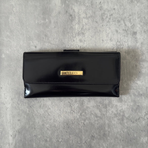 Gucci Continental Wallet in black patent leather, featuring a gold-tone Gucci logo, multiple card slots, and a spacious interior, epitomizes luxury and functionality.