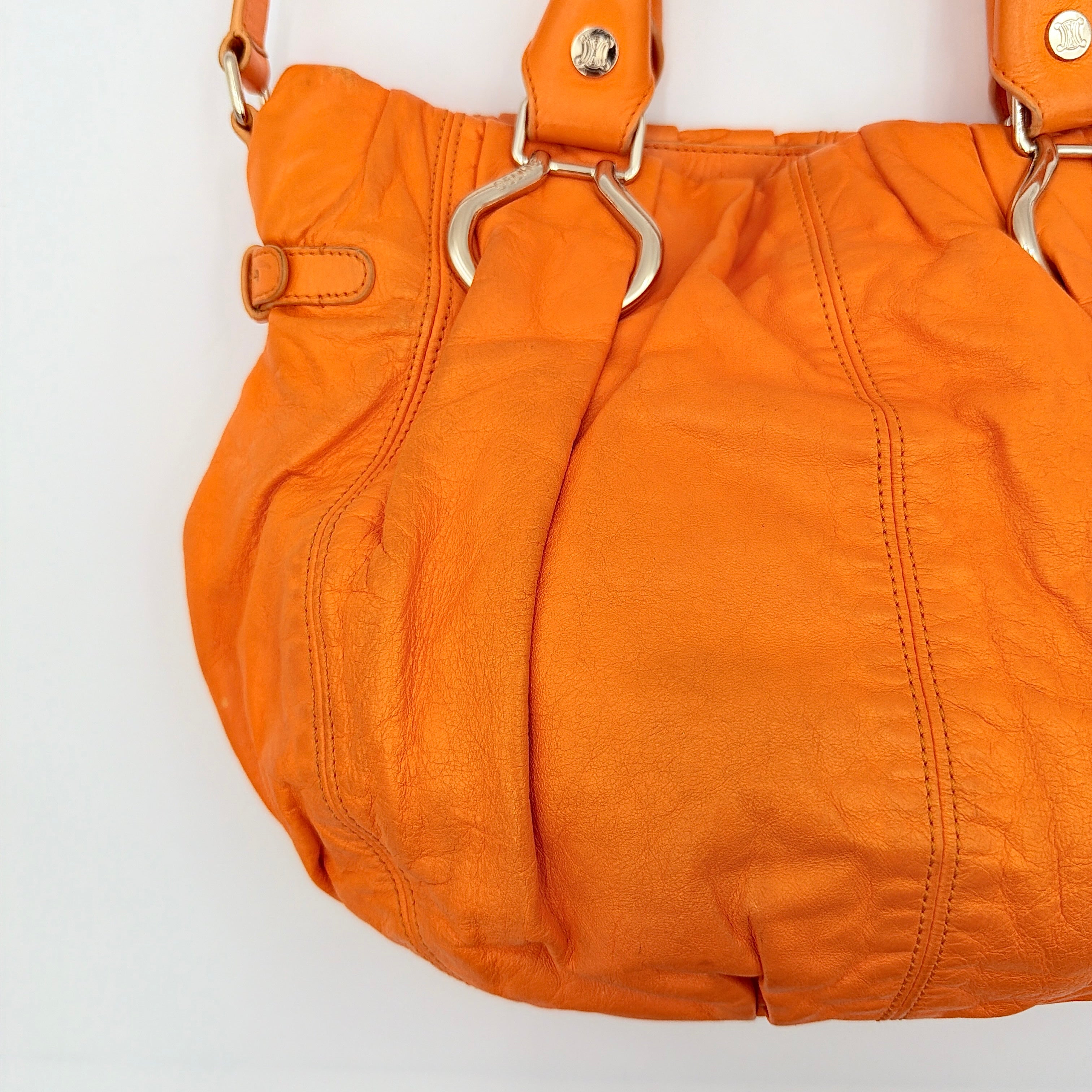 Celine 2Way Shoulder Bag in vibrant orange leather with silver-tone hardware and pleated detailing, shown with both top handles and an adjustable strap.