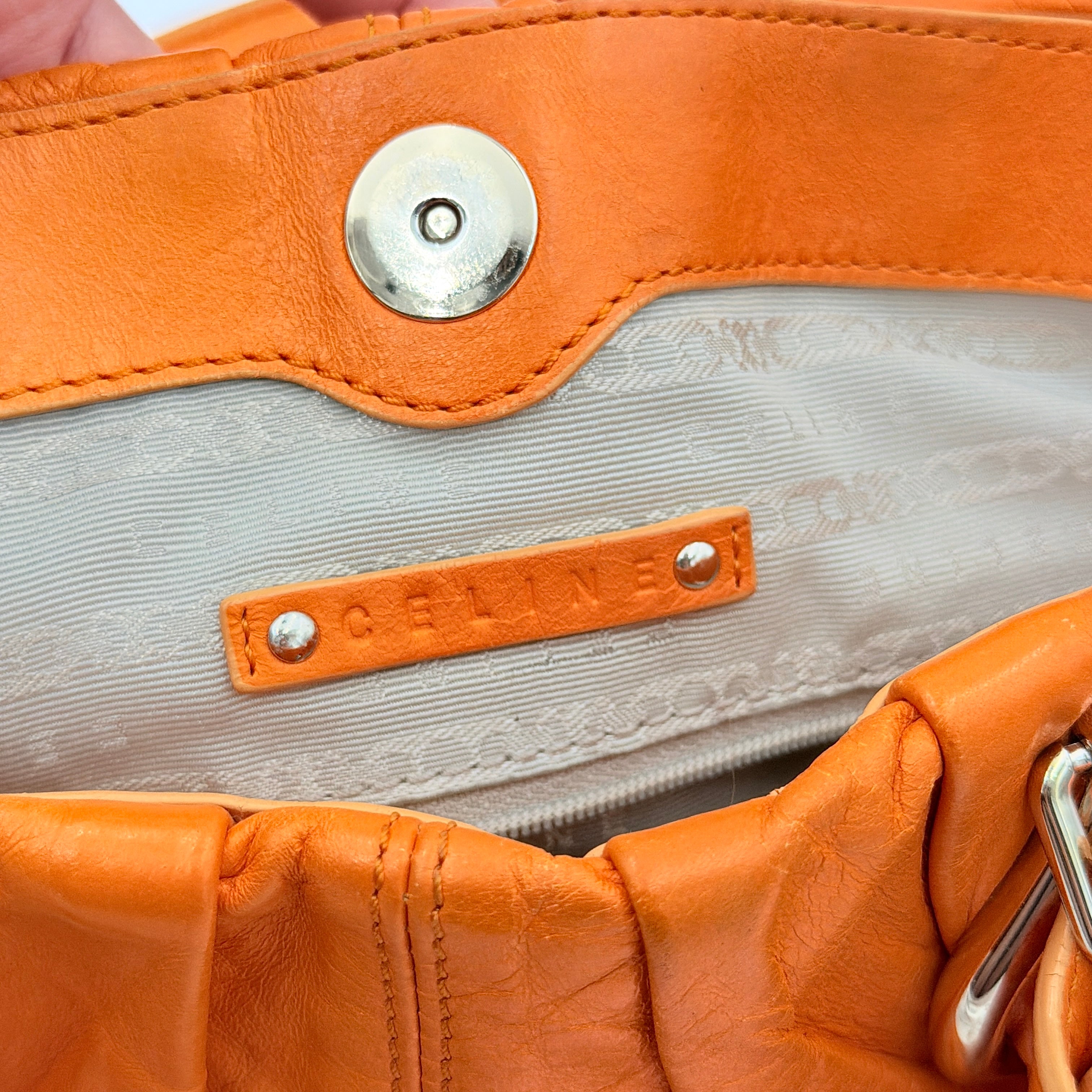 Celine 2Way Shoulder Bag in vibrant orange leather with silver-tone hardware and pleated detailing, shown with both top handles and an adjustable strap.
