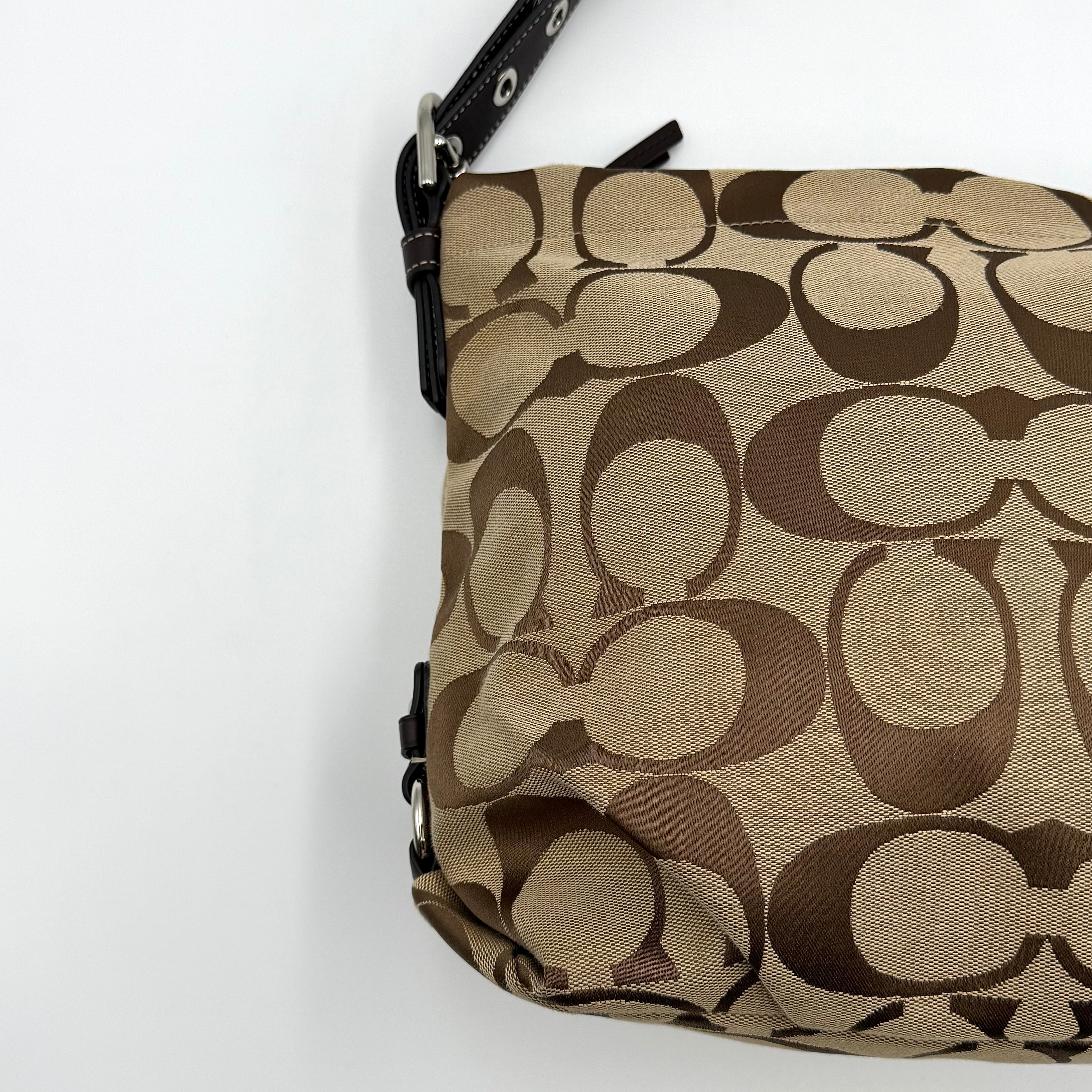 Coach beige and brown signature canvas hobo shoulder bag with black leather strap and silver hardware shown on a white background.