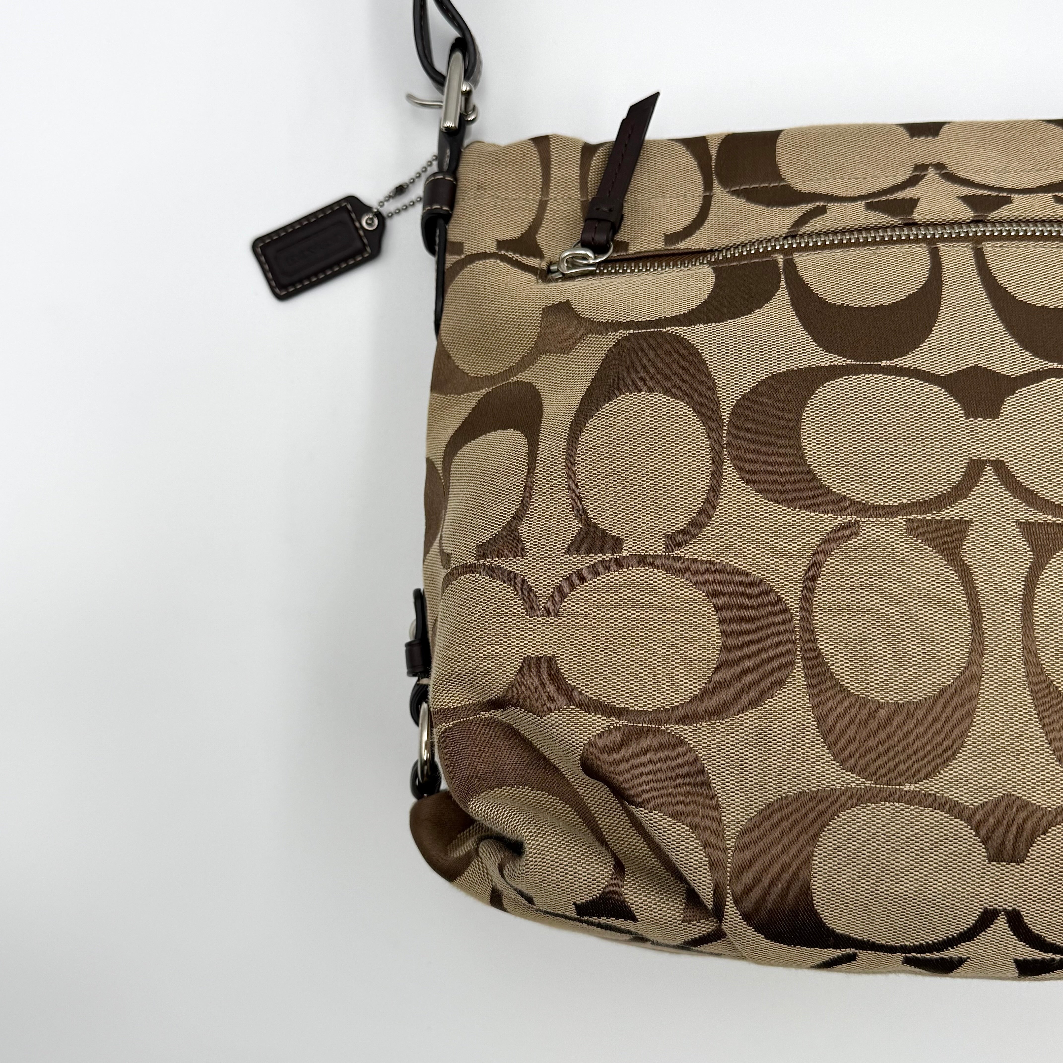 Coach beige and brown signature canvas hobo shoulder bag with black leather strap and silver hardware shown on a white background.