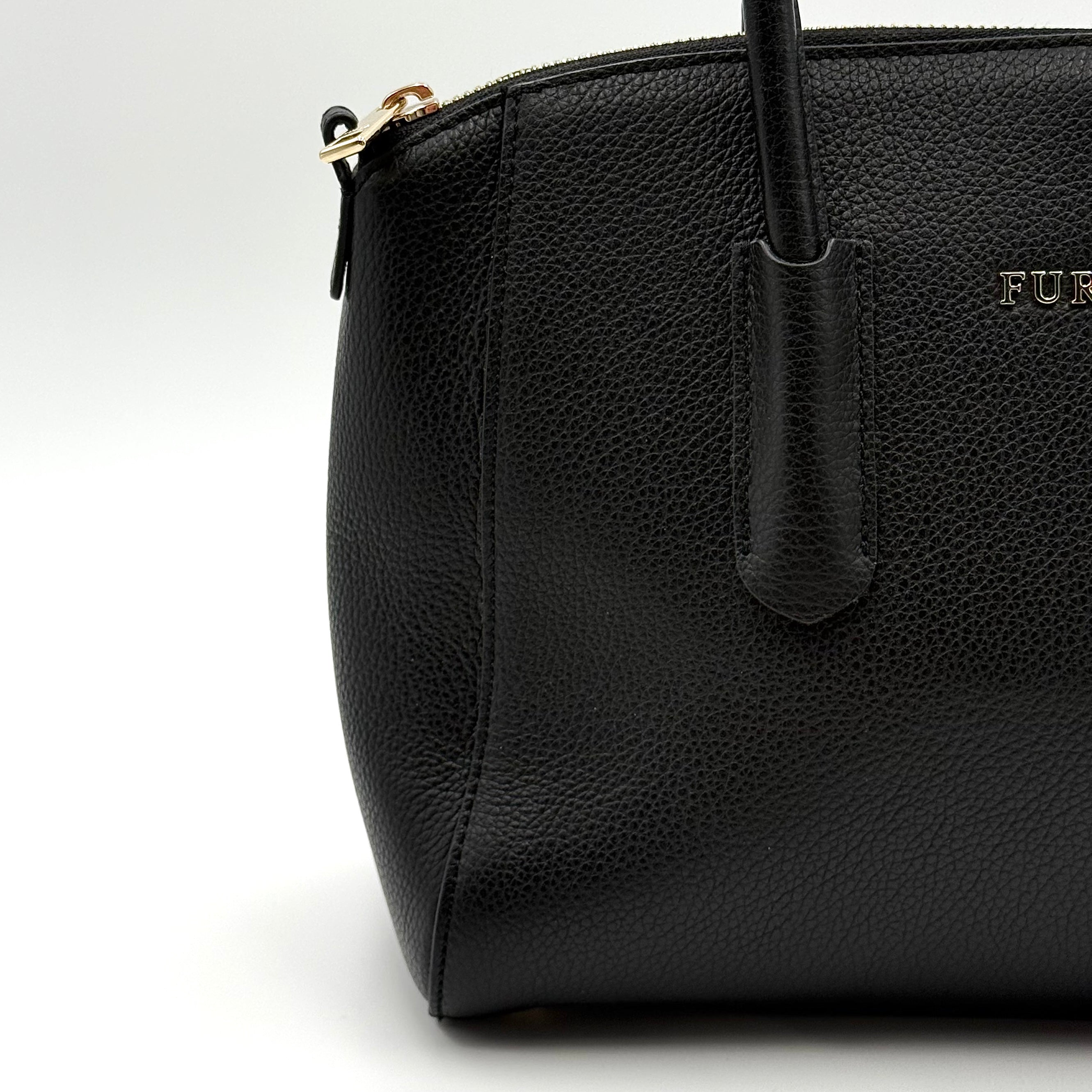 Front view of the Furla Tessa black leather satchel with gold-tone Furla charm and structured silhouette.
