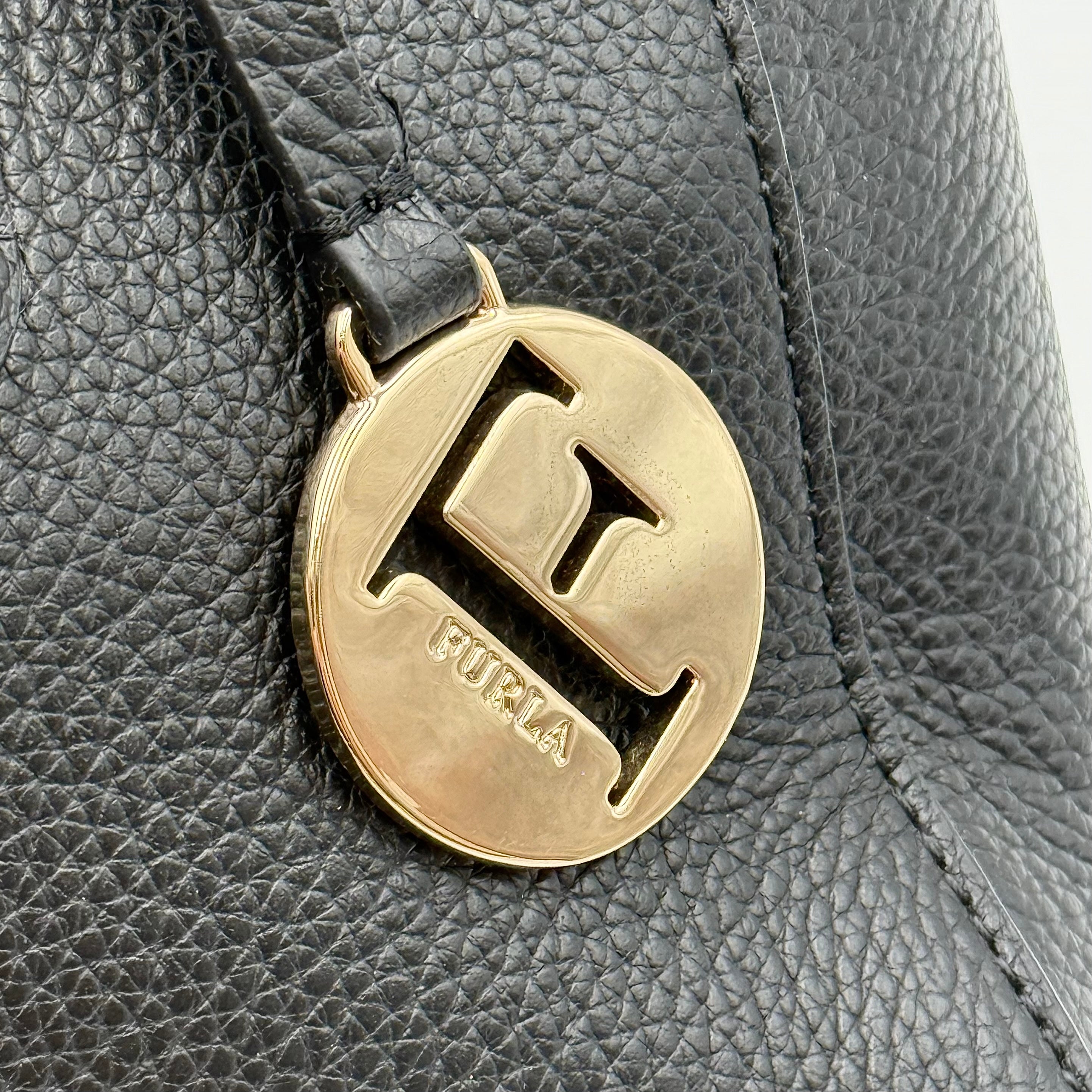 Front view of the Furla Tessa black leather satchel with gold-tone Furla charm and structured silhouette.