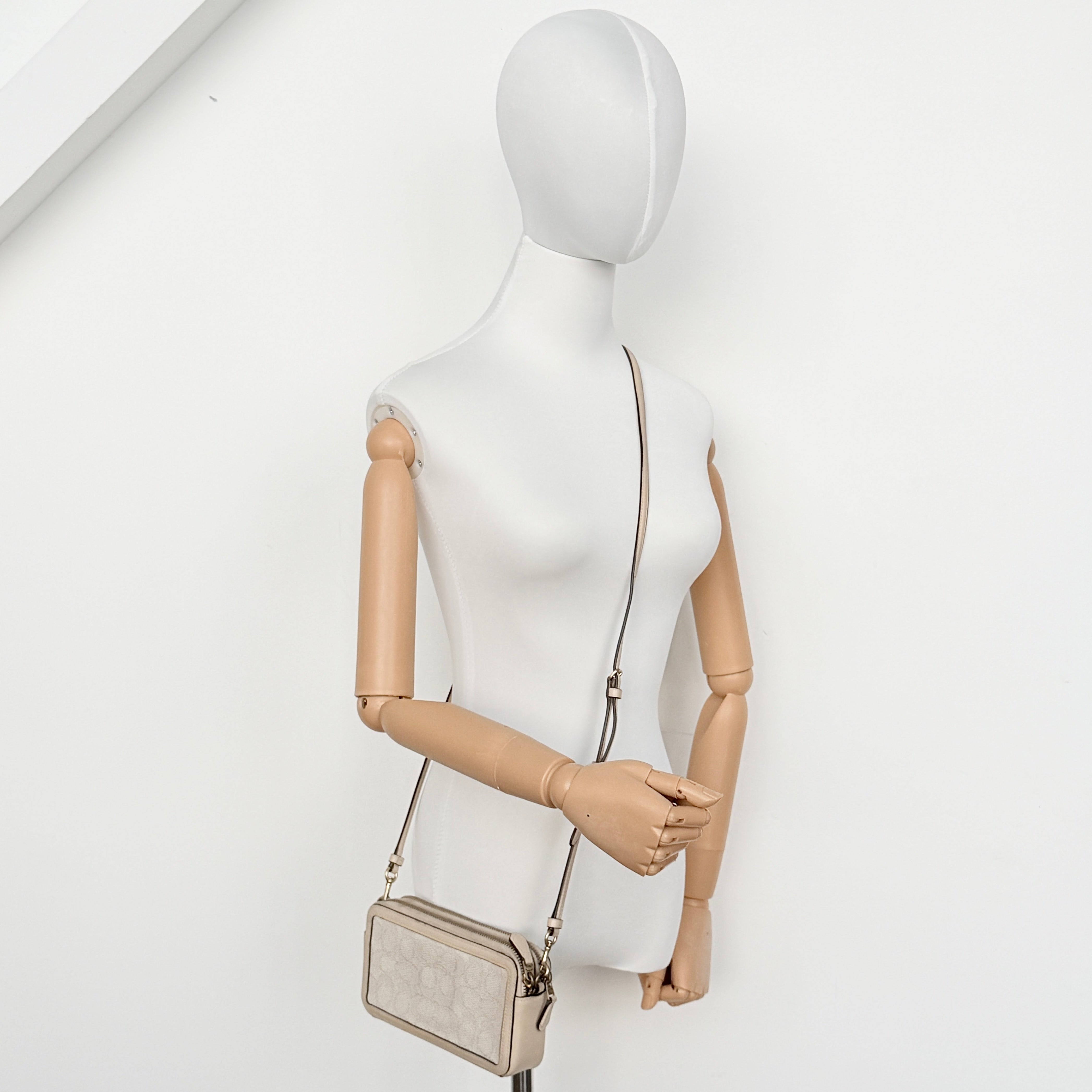 Coach Signature Kira Crossbody Bag in beige and white jacquard with leather trim and adjustable strap displayed against a white background.