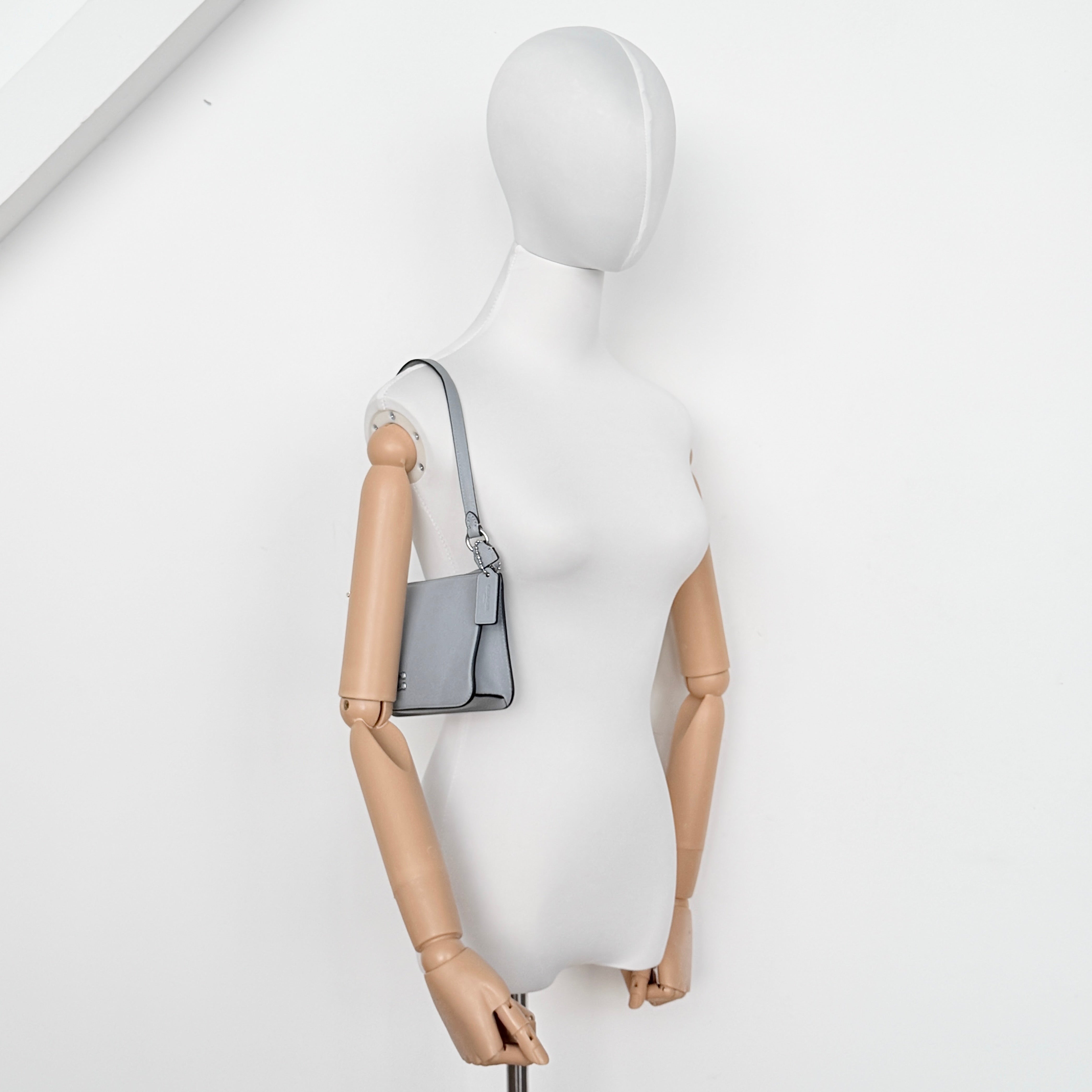 Sky blue Coach grained leather shoulder bag with silver-tone C plaque and short strap, displayed against a white background.