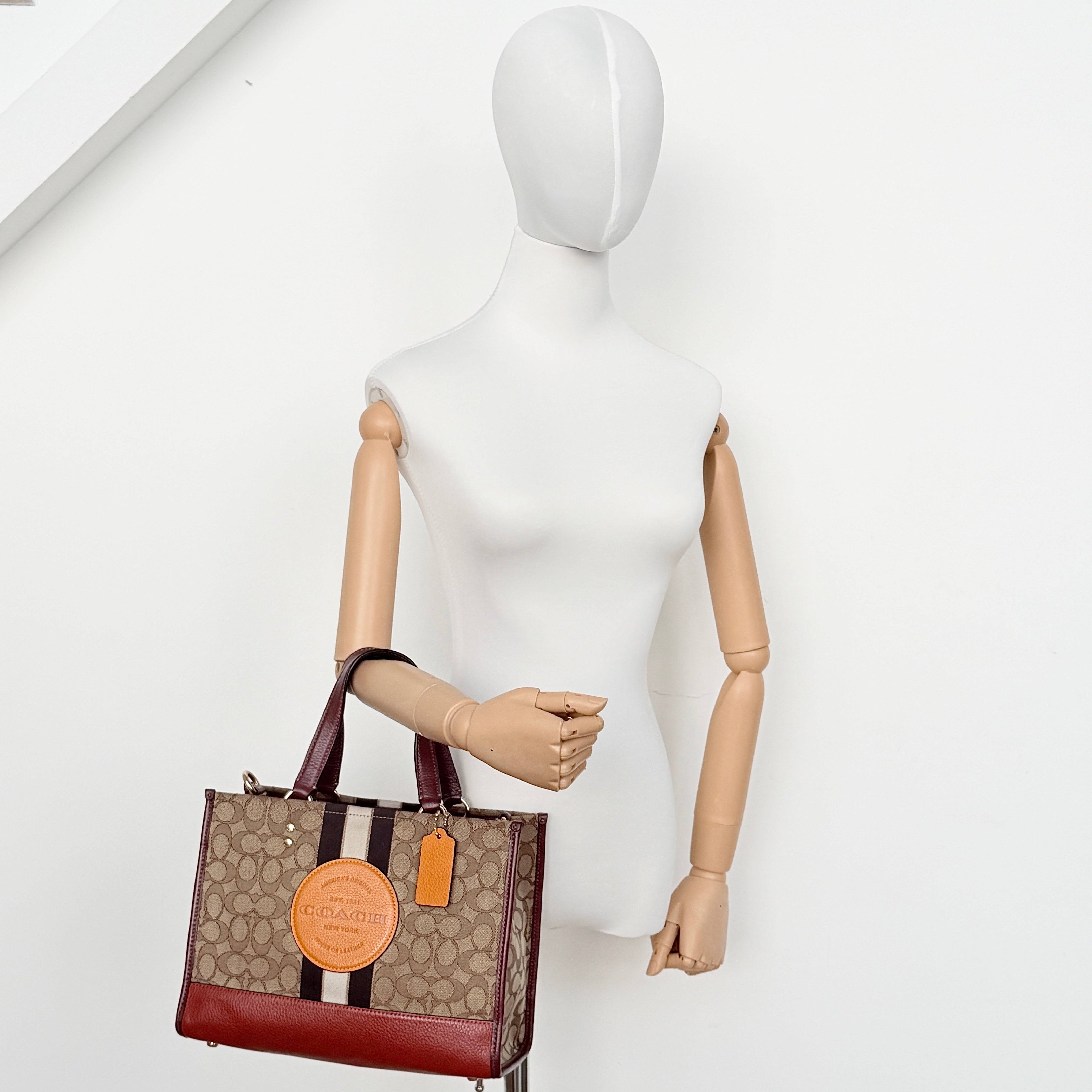 Coach 2Way Signature 22 Dempsey Tote in brown jacquard and burgundy leather with orange logo patch, shown with detachable strap.