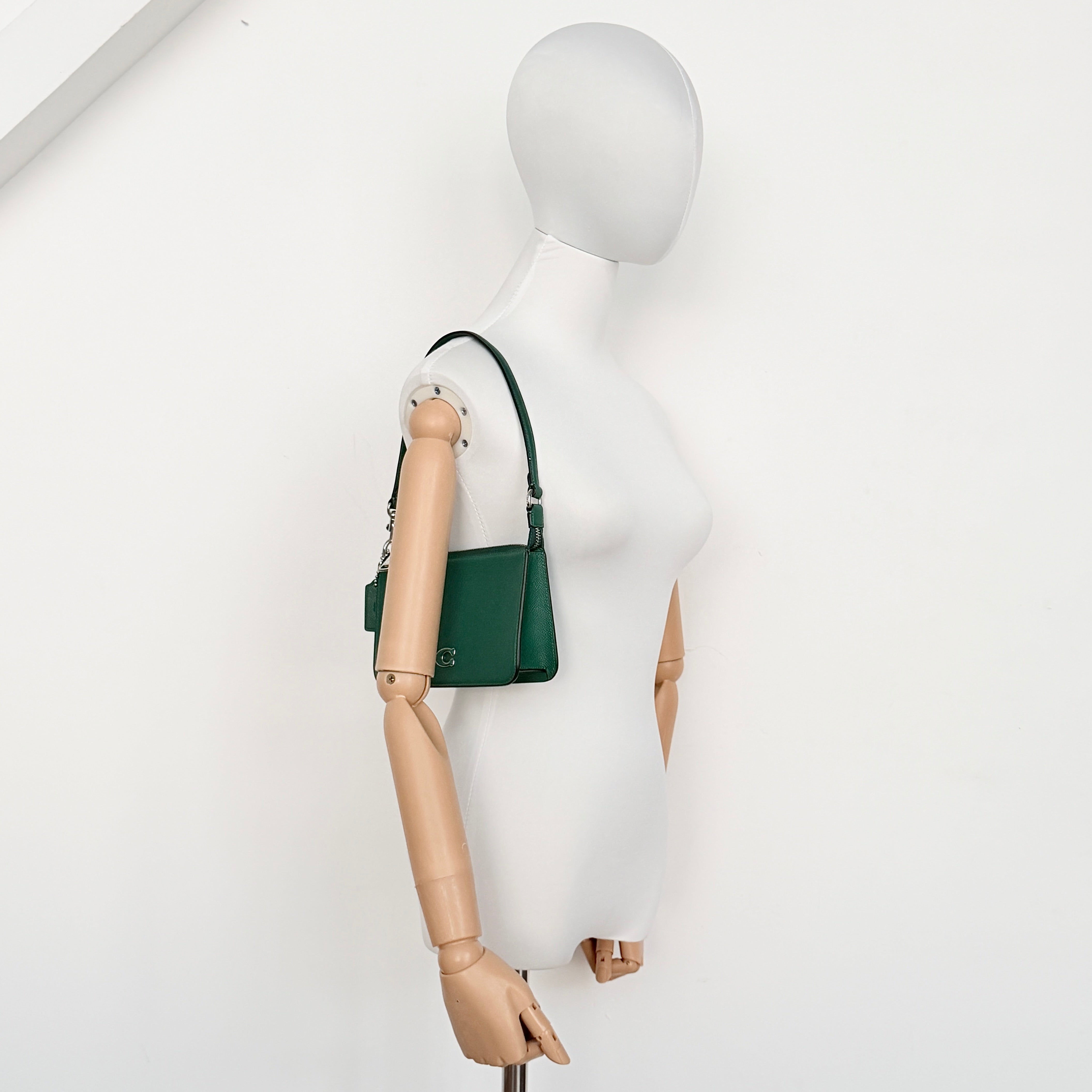 Coach green grained leather shoulder bag with silver C plaque and top zip, styled with a short strap.