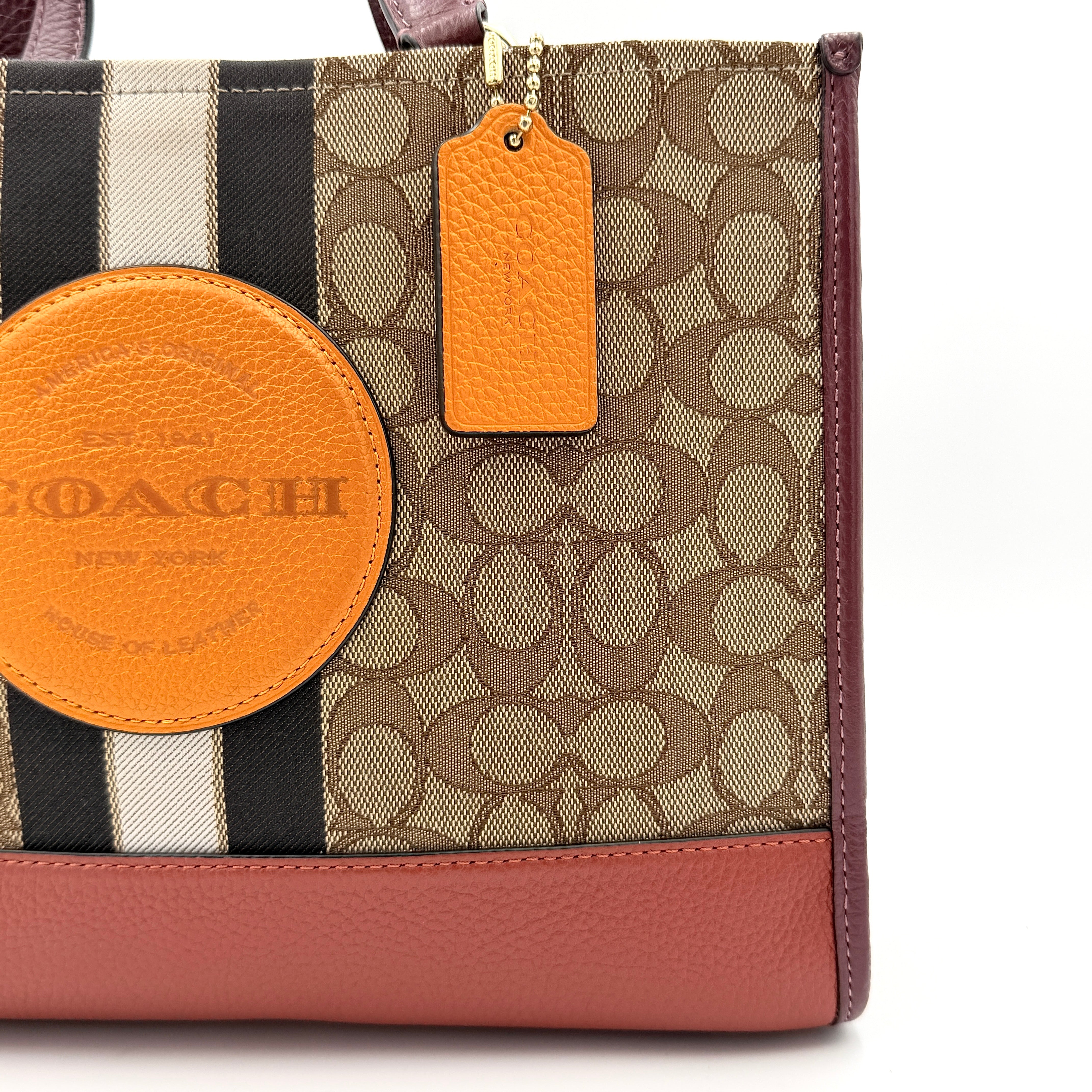Coach 2Way Signature 22 Dempsey Tote in brown jacquard and burgundy leather with orange logo patch, shown with detachable strap.